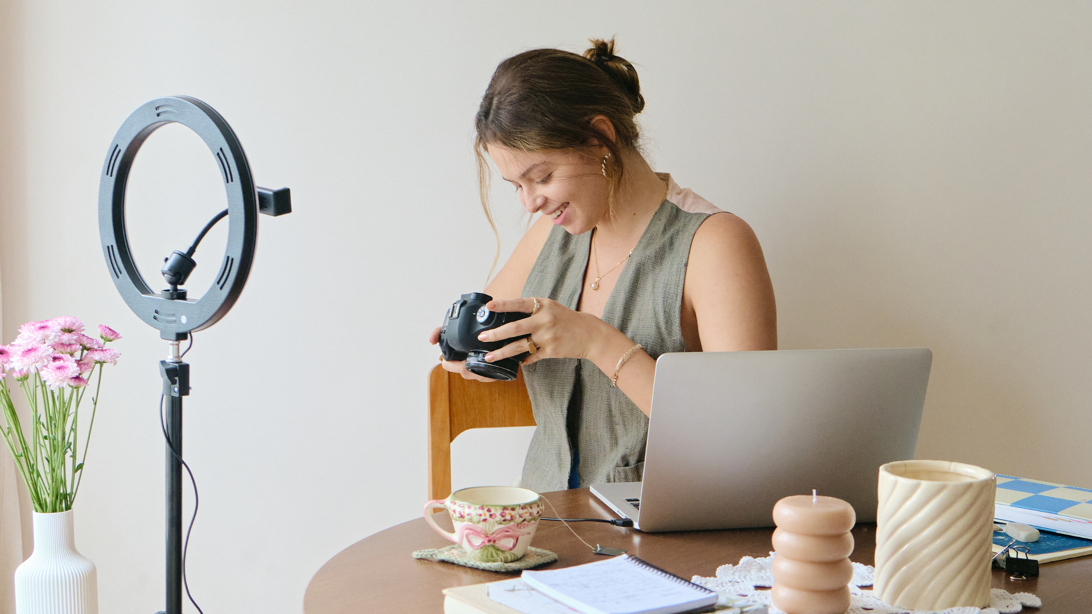 Behind the Scenes: Creator at Work Woman at a desk smiling while setting up a camera, with a ring light, laptop, and coffee nearby.