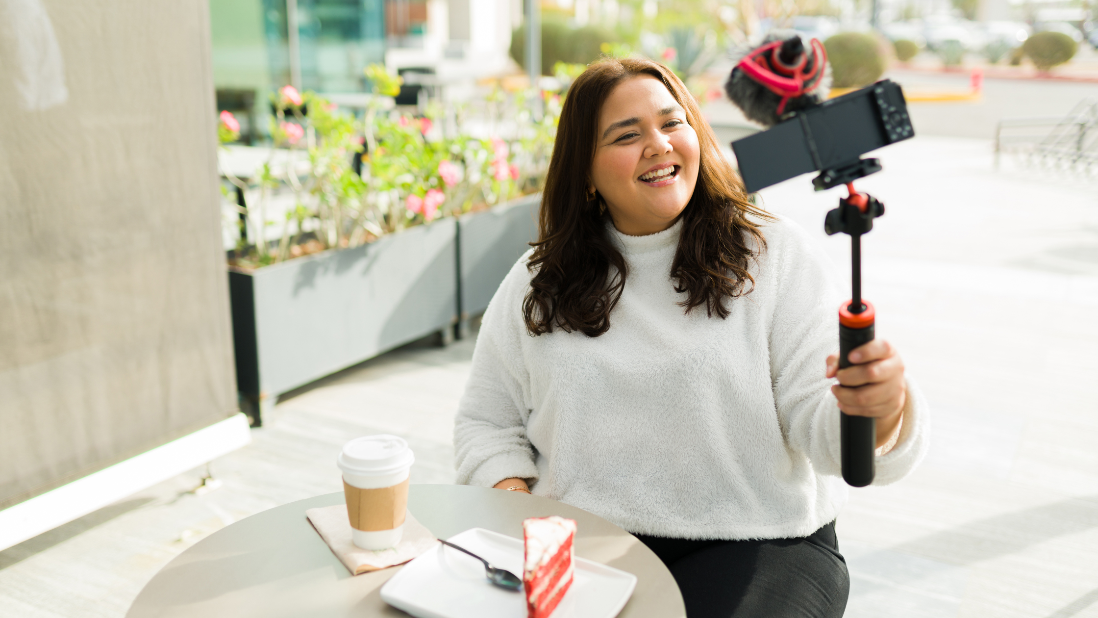 Vlogger Recording Outdoor Lifestyle Content With Coffee and Cake Smiling woman recording vlog at outdoor cafe with coffee and dessert