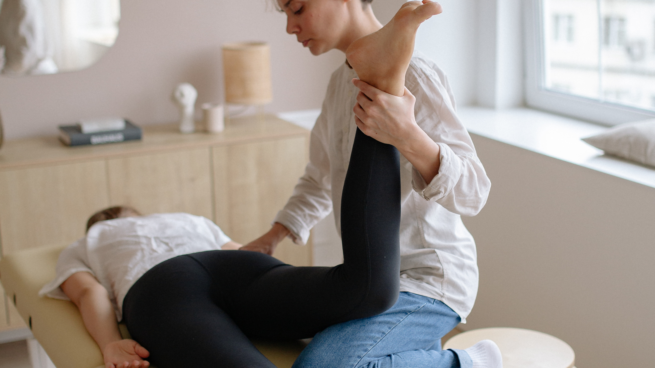 Targeted Leg Mobility Therapy Session Therapist performing a leg mobility exercise on a patient lying face down on a treatment table.