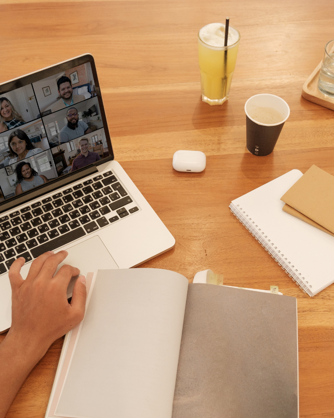 Laptop showing a remote marketing team on a video call with notebooks and drinks on a wooden desk