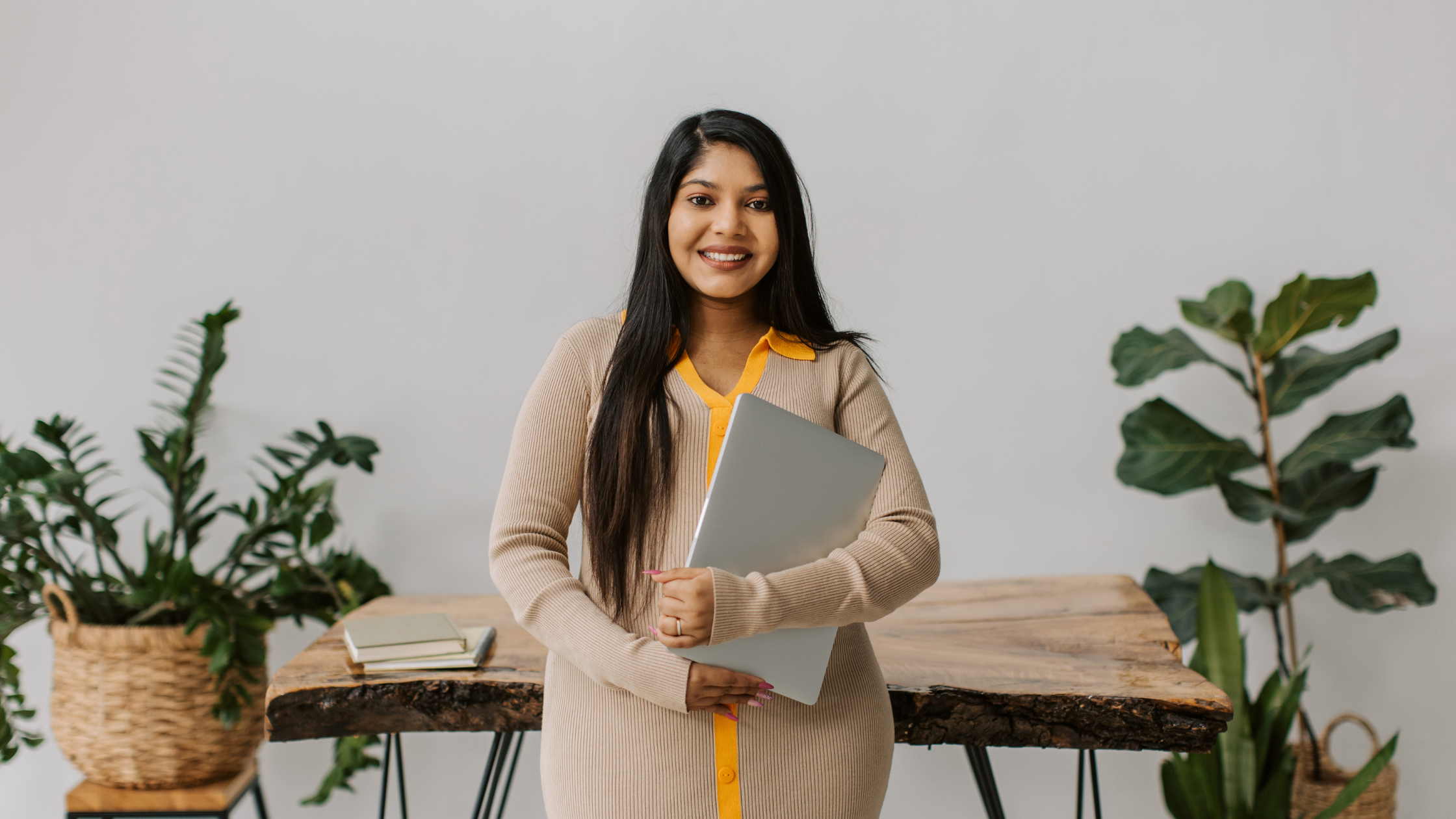 Woman Entrepreneur Holding Laptop in Natural Workspace Professional woman standing confidently while holding a laptop in a creative office environment