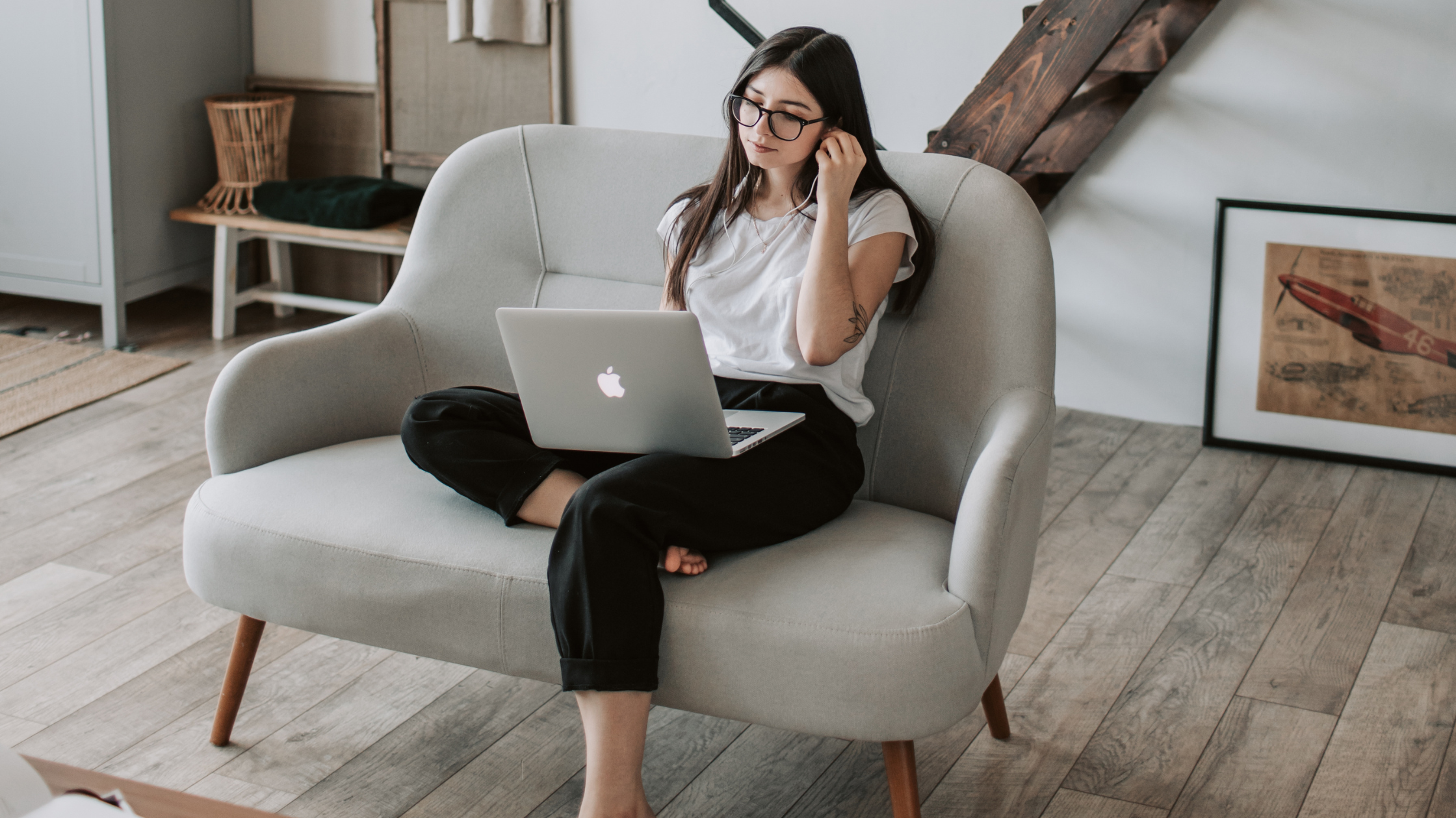 Woman working from sofa with laptop and earphones Woman sitting on sofa with laptop and earphones in a modern living room