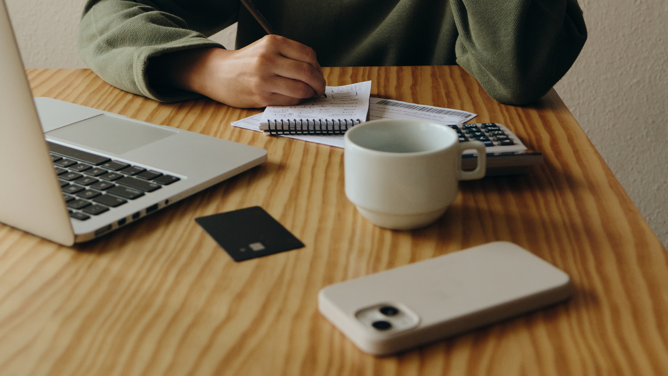 Close-up of a person writing notes next to a laptop and phone, representing the planning of key messaging and social media content.