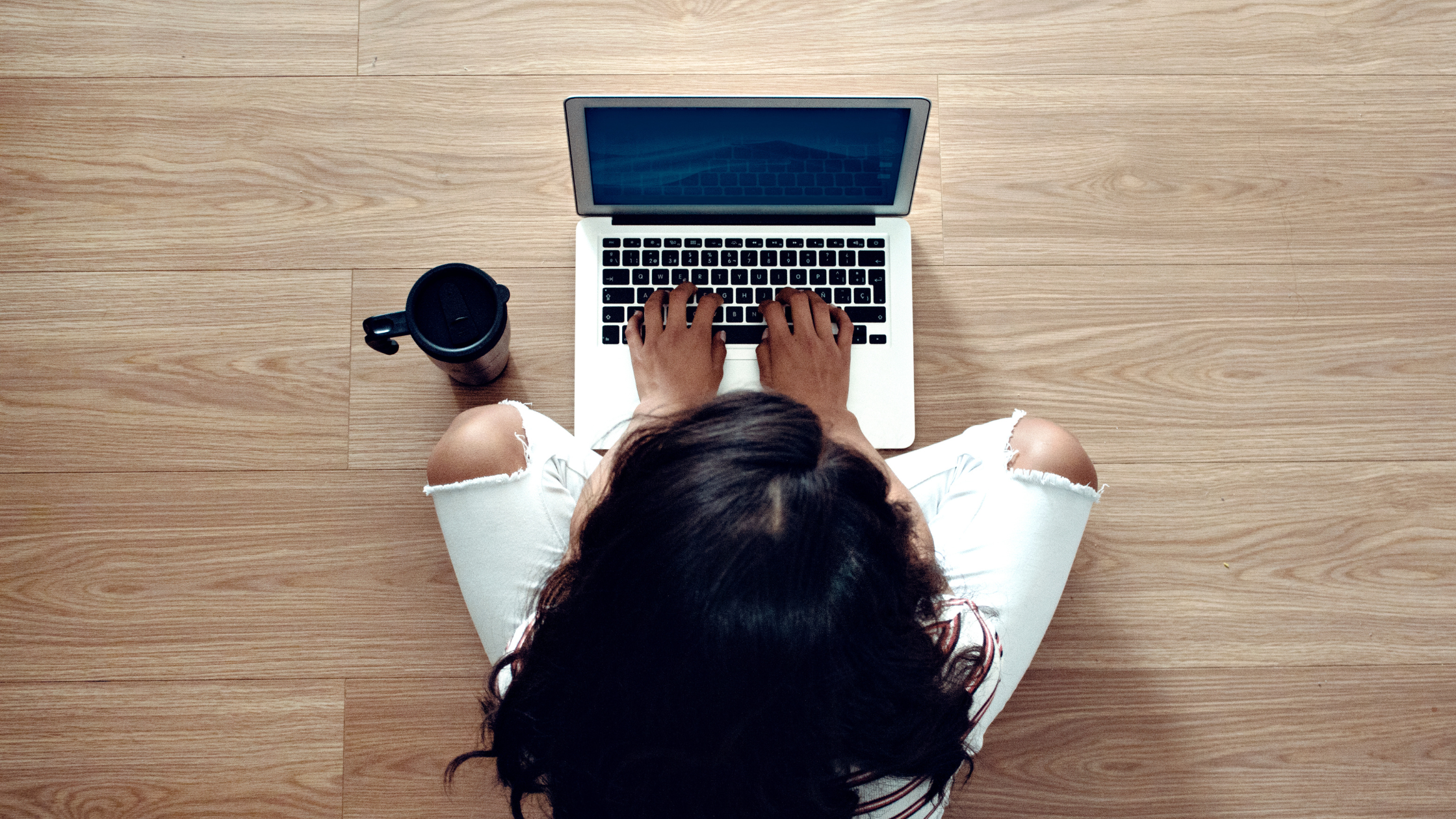 Overhead view of a woman typing on a laptop while seated cross-legged, symbolizing content creation for customer education on social media.