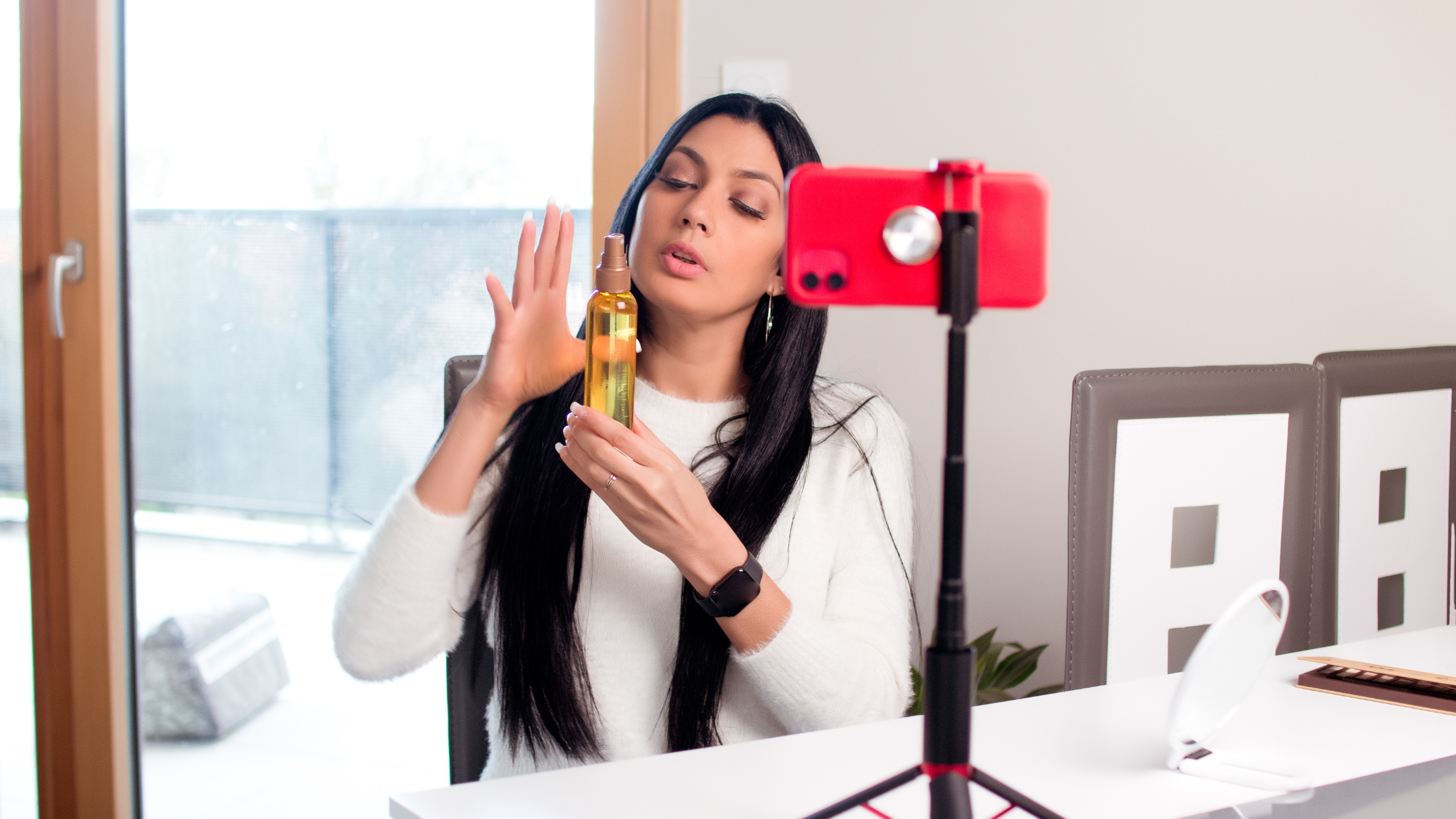 Female influencer filming product review with smartphone on tripod at home.