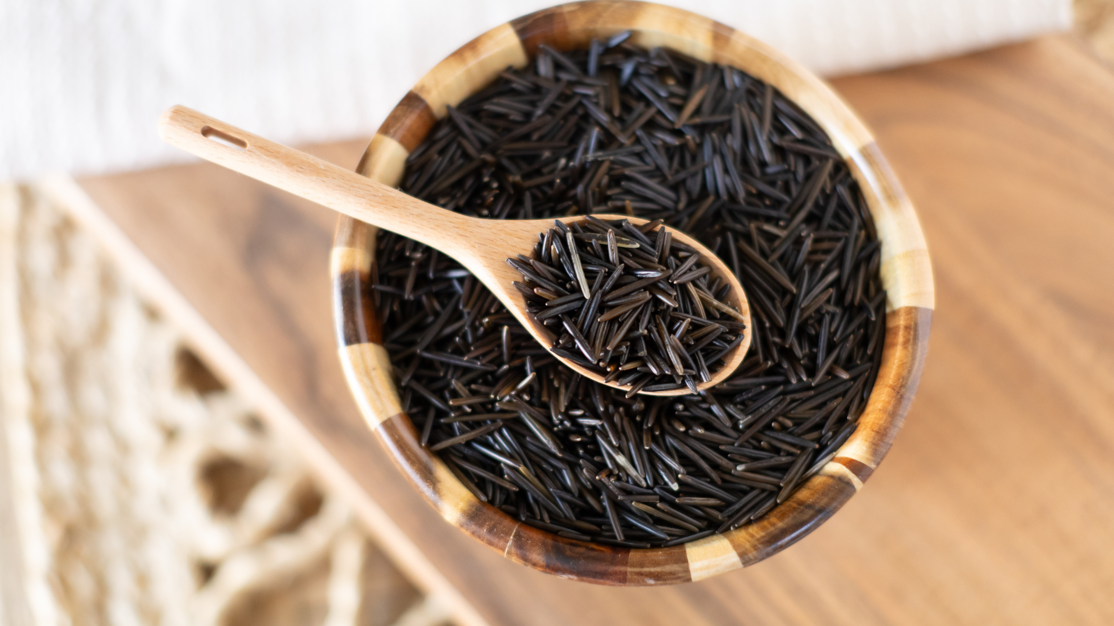 Raw Wild Rice with Wooden Spoon Wooden spoon scooping raw wild rice from a bowl.