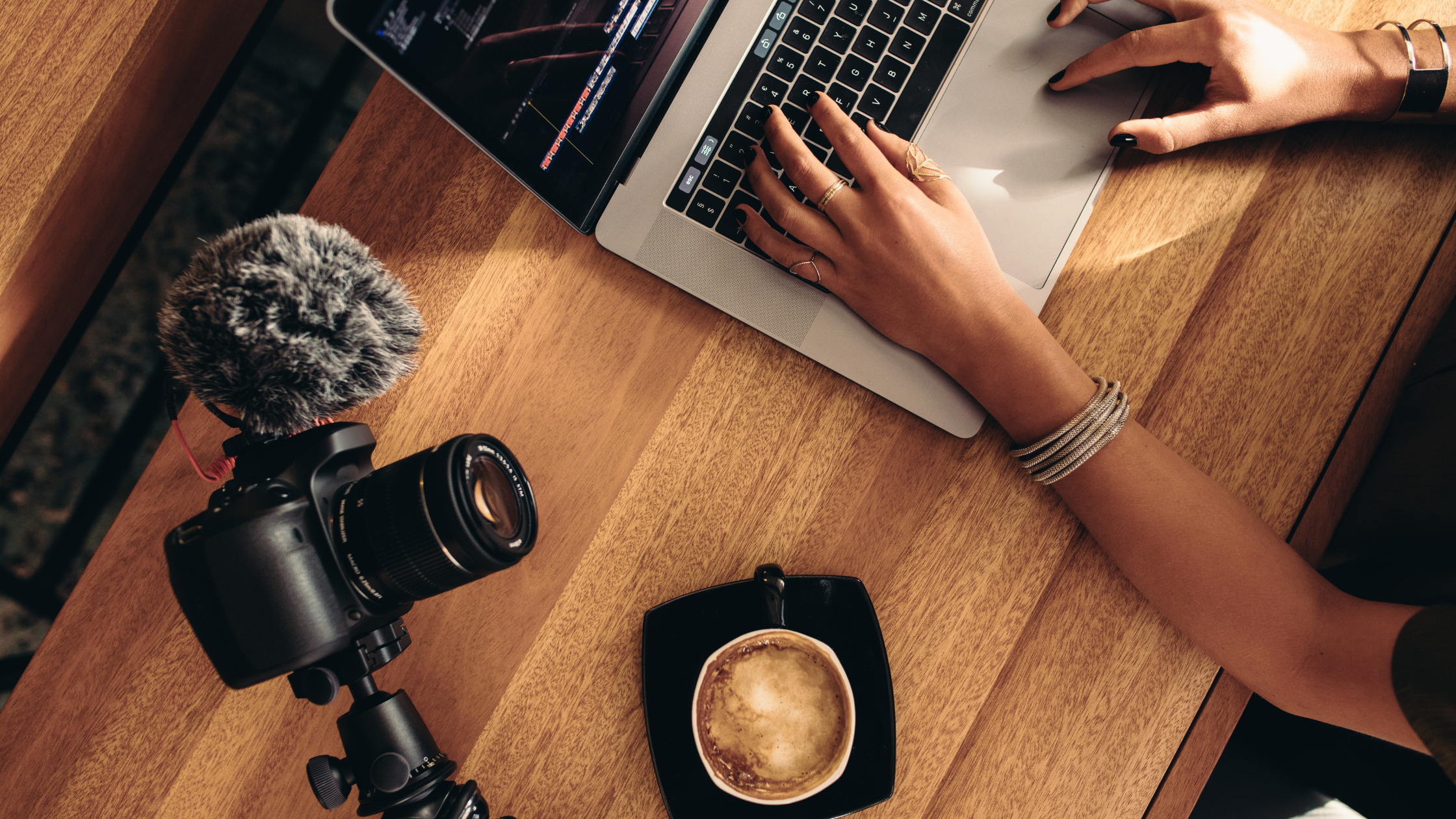 Filming Setup for Content Creators Camera with microphone and laptop on wooden table beside a coffee cup, representing a creator’s filming and video editing setup.