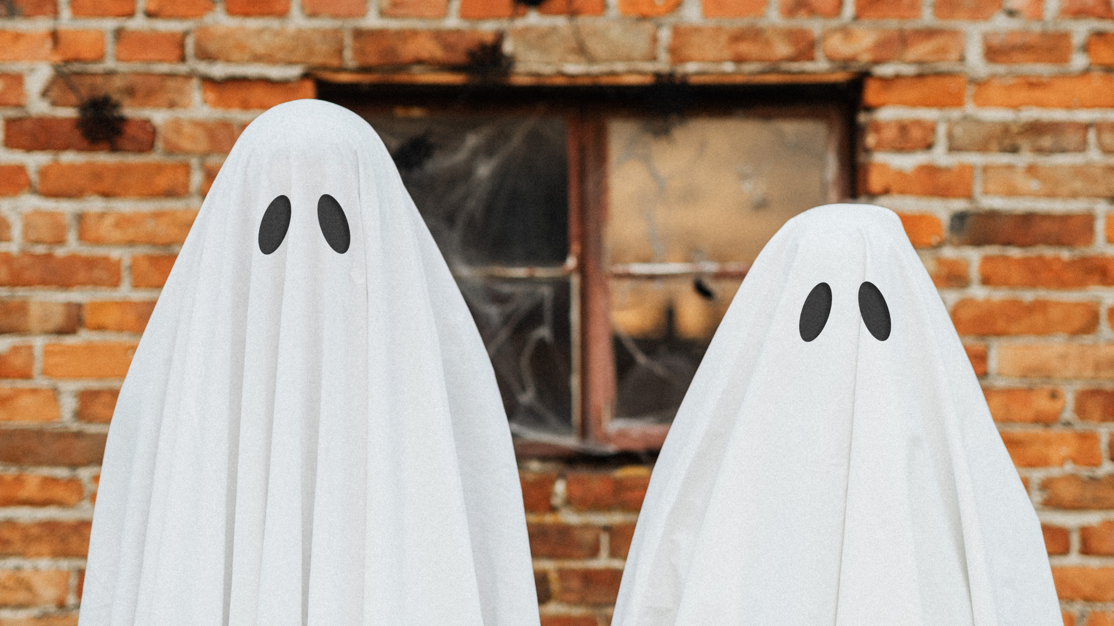 Ghosting Your Audience Concept Two people dressed as ghosts standing in front of a brick wall with cobwebs on a window.