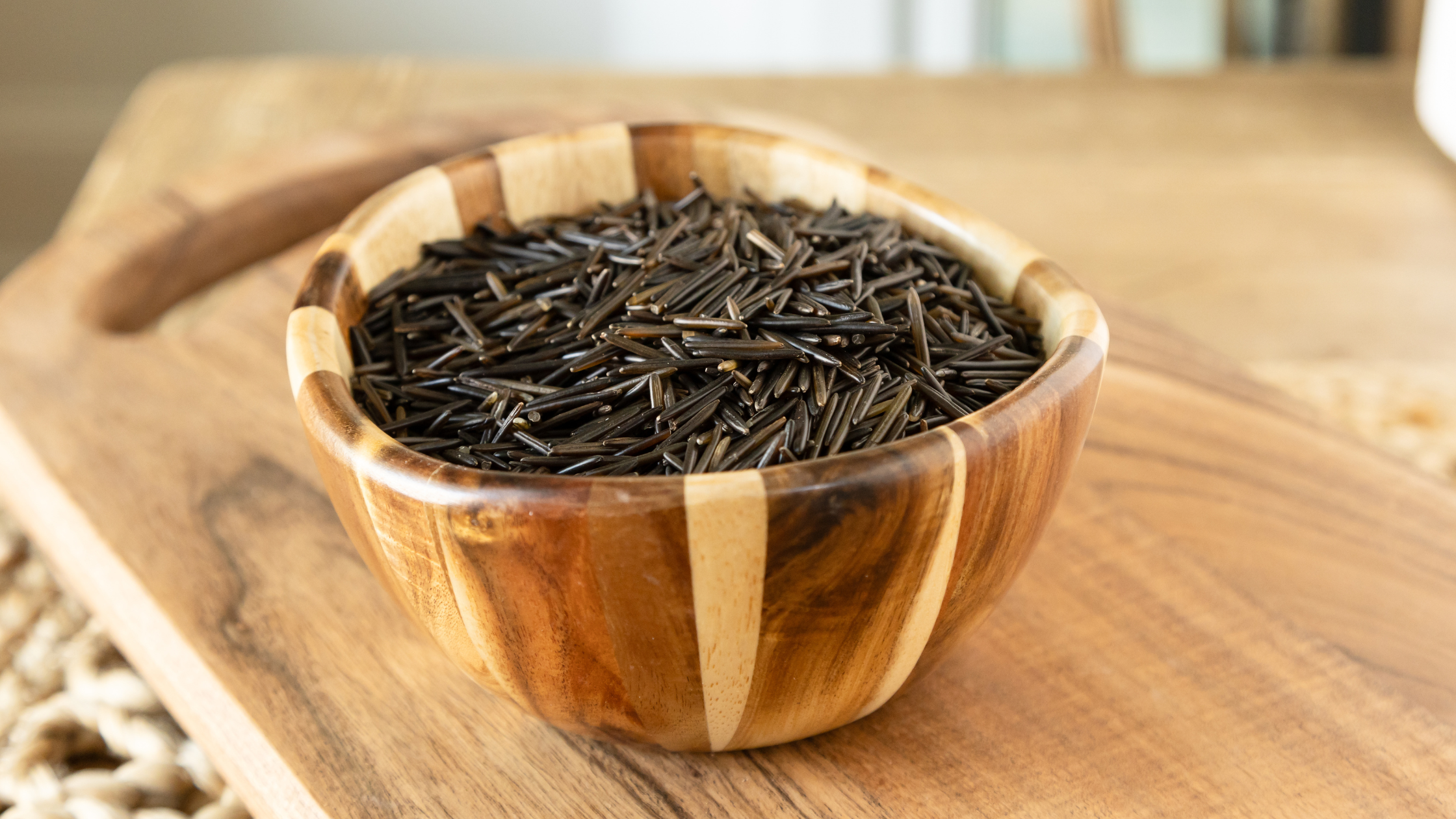 Uncooked wild rice in a wooden striped bowl on a cutting board.