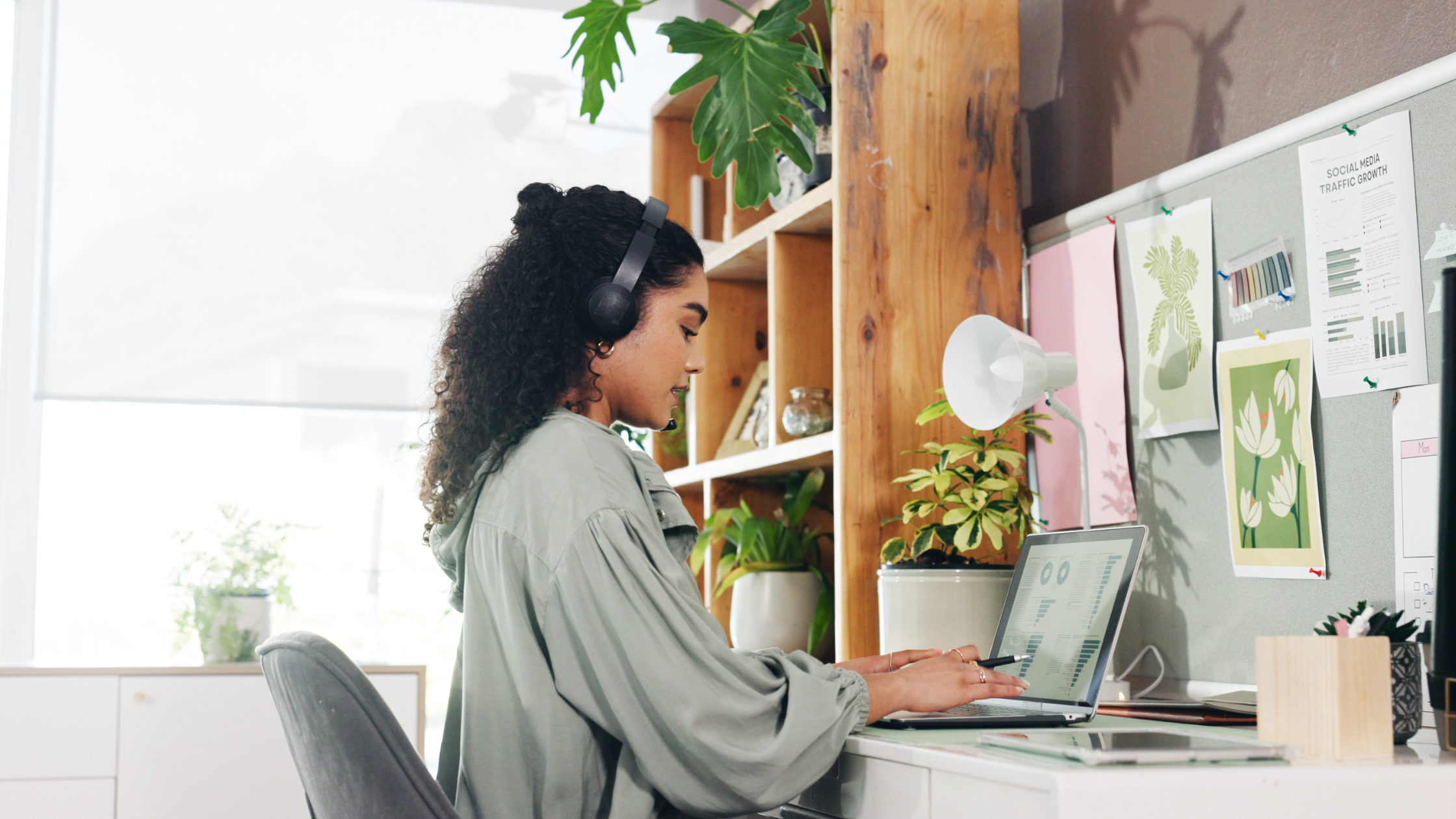 Woman working on laptop with headphones in a bright workspace, analyzing social media growth data.