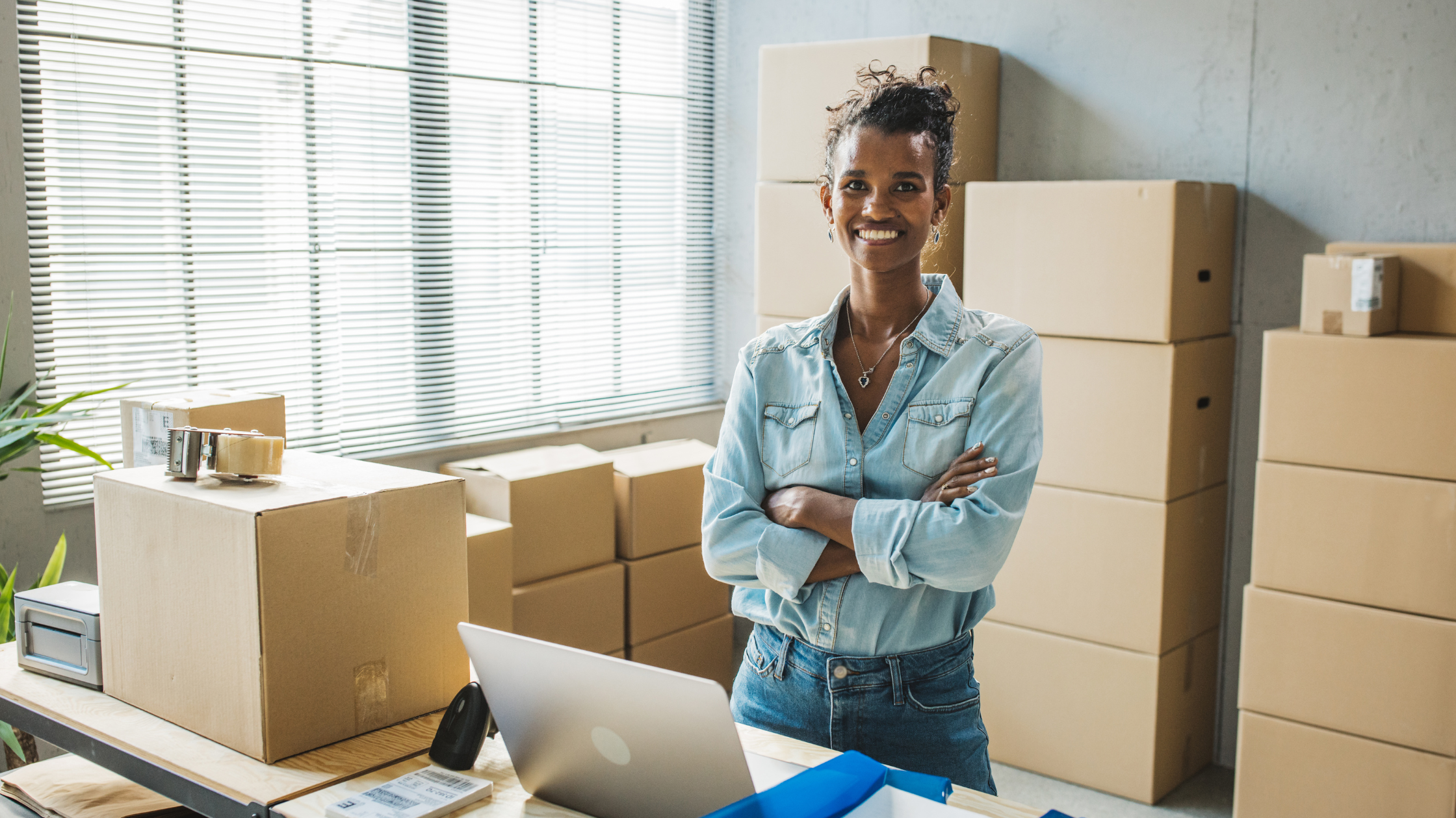 Small business owner standing confidently in a workspace filled with shipping boxes.