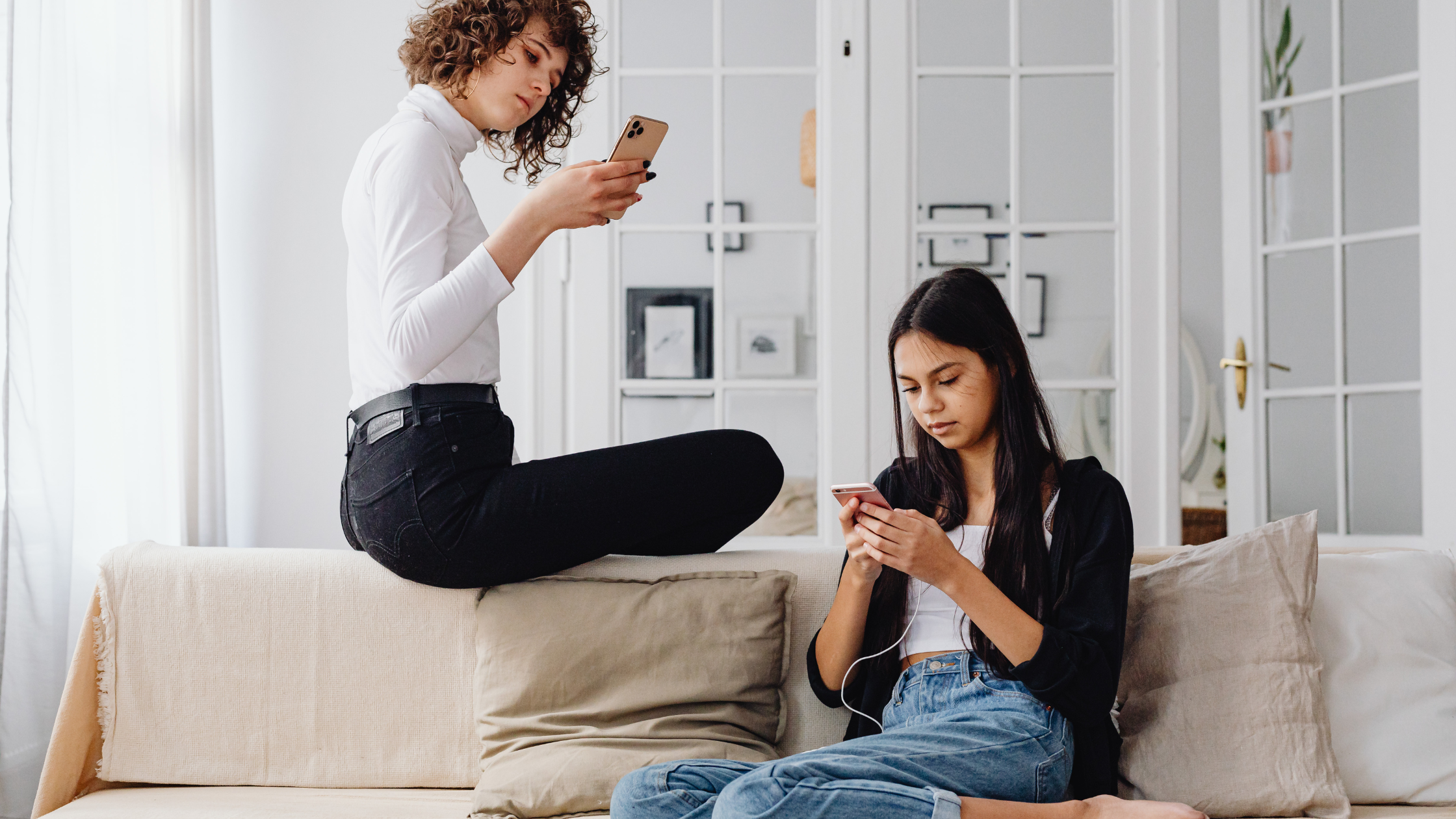 Two young women sitting on a couch, each focused on their phones while browsing social media.