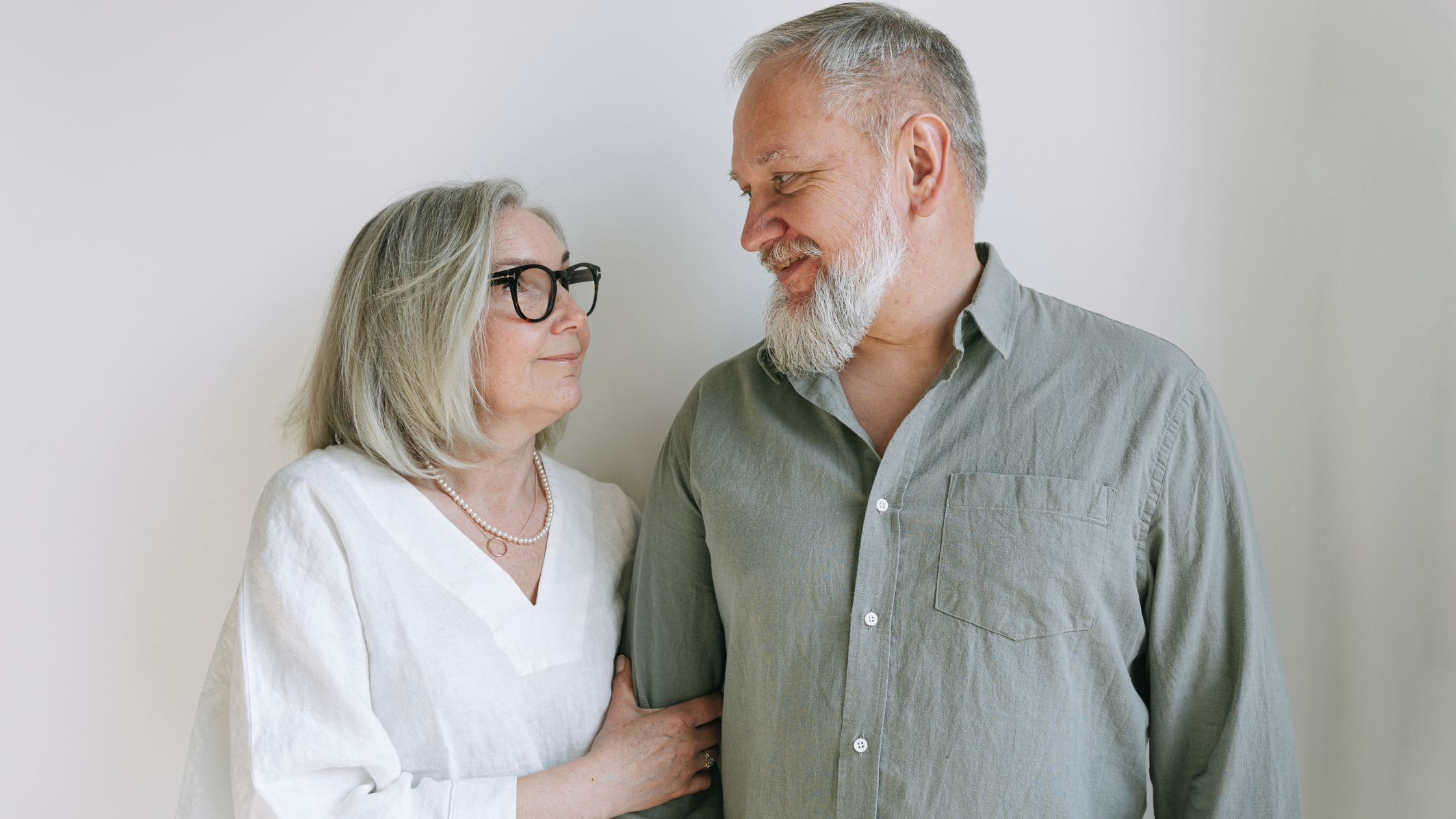 Older couple over 60 smiling at each other in a calm, neutral indoor setting