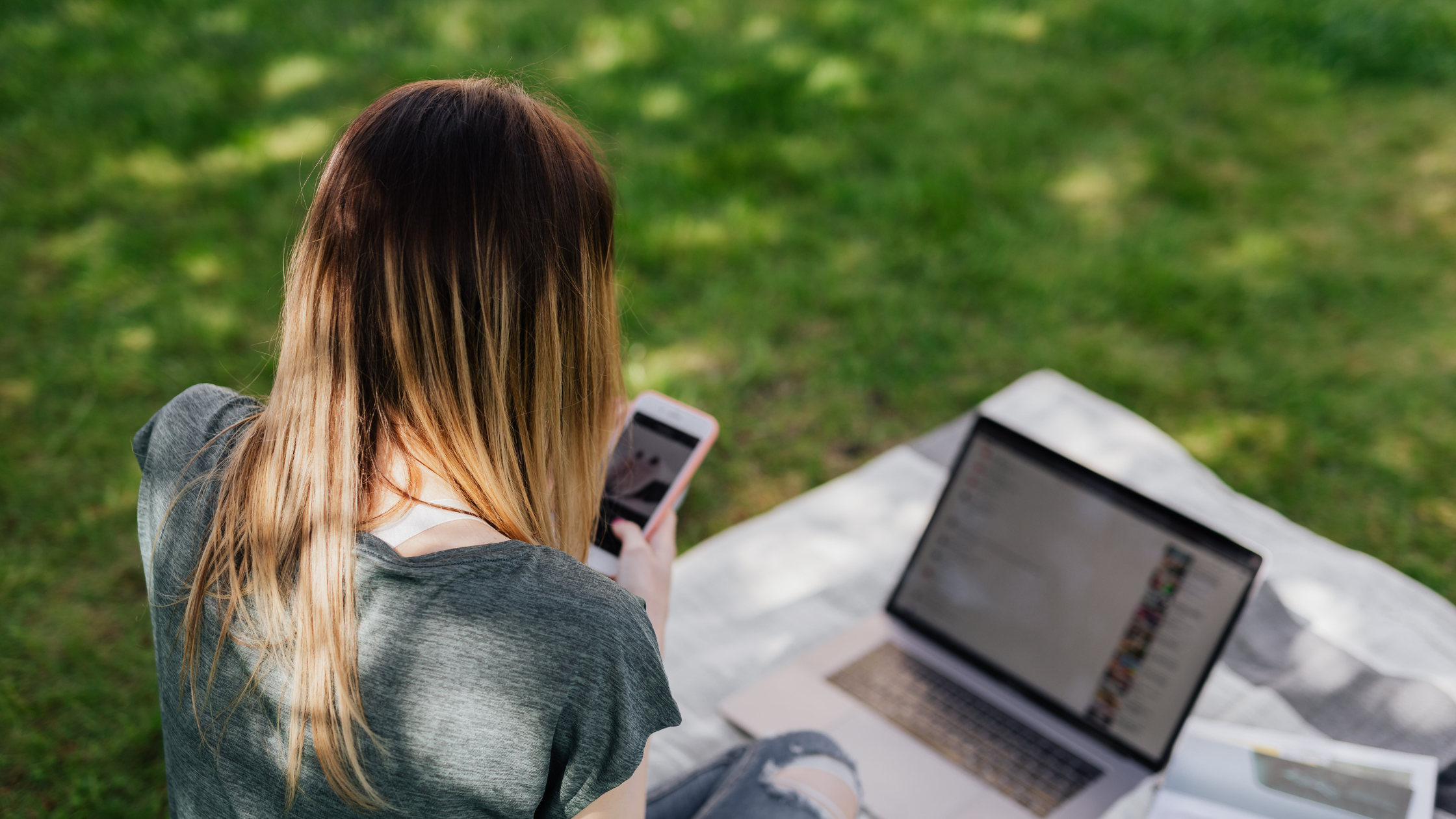 Woman working on social media outdoors with laptop and phone, highlighting modern outsourced social media workflows