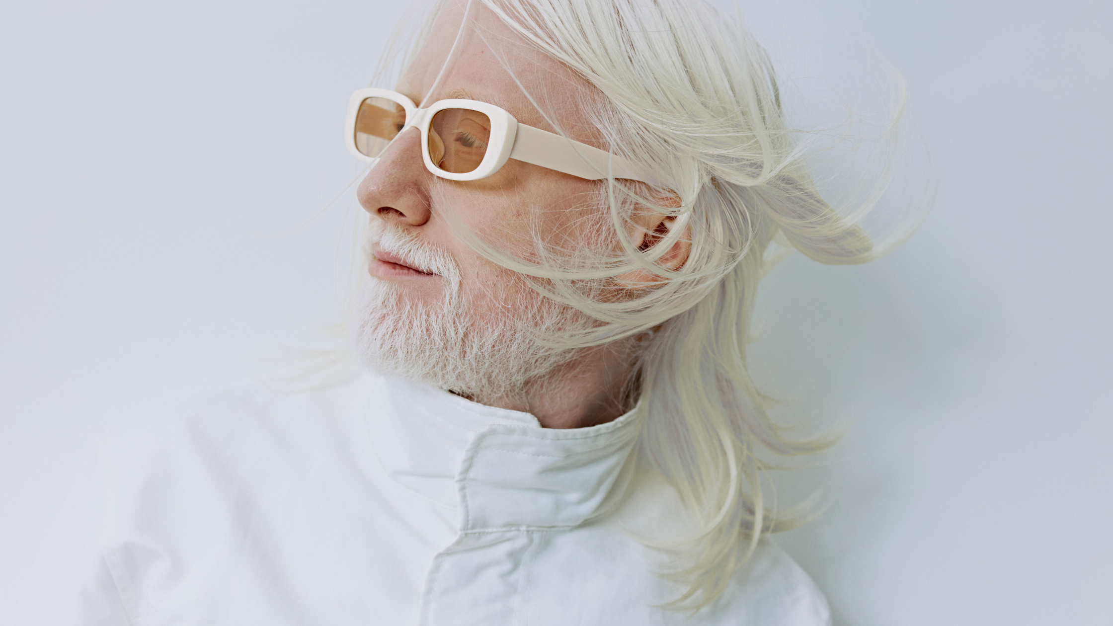 Stylish older adult with white hair and beard wearing sunglasses in a clean, modern setting