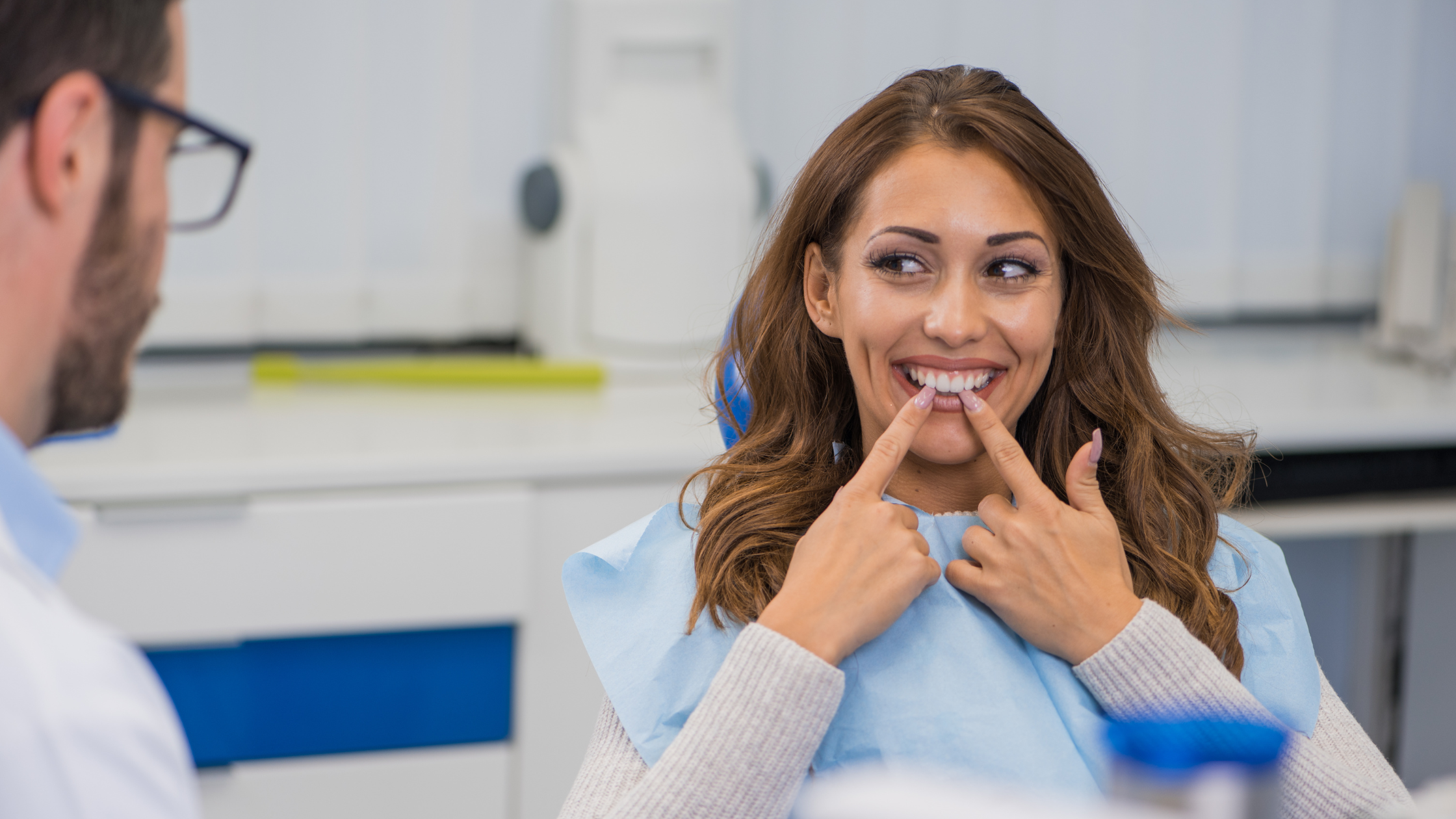 Smiling patient pointing at teeth after dental treatment consultation