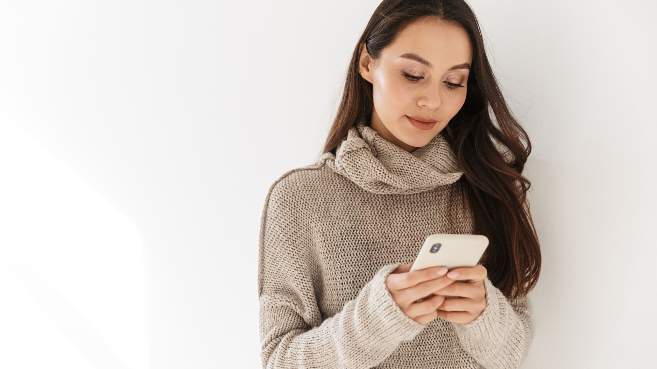 Woman in neutral sweater looking at her phone, representing thoughtful social media use