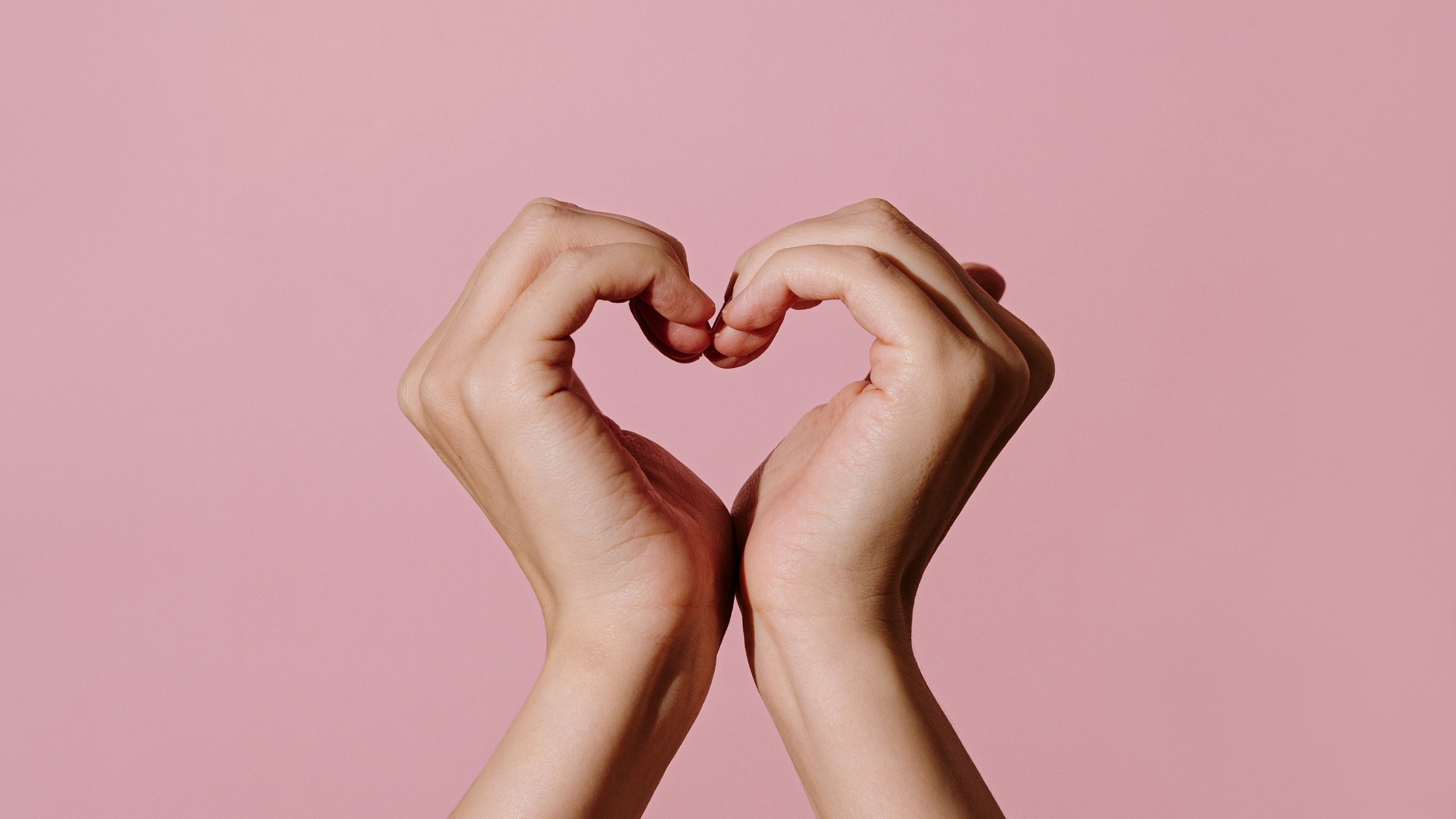 Hands forming heart shape on pink background symbolizing connection and engagement