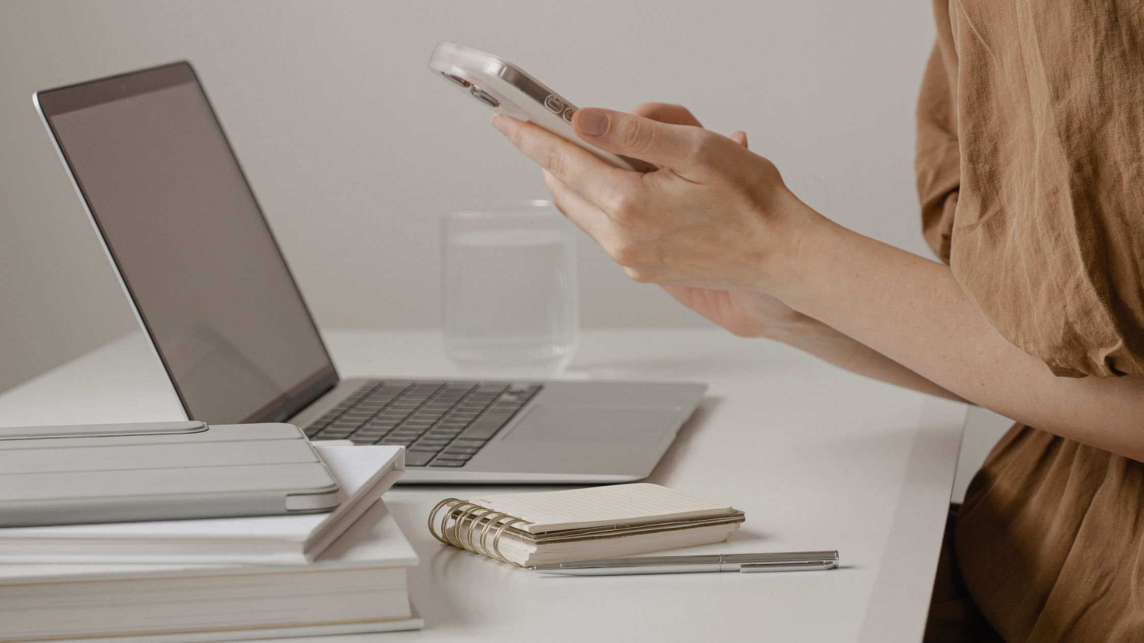 Person using smartphone at desk with laptop and notebook for content planning