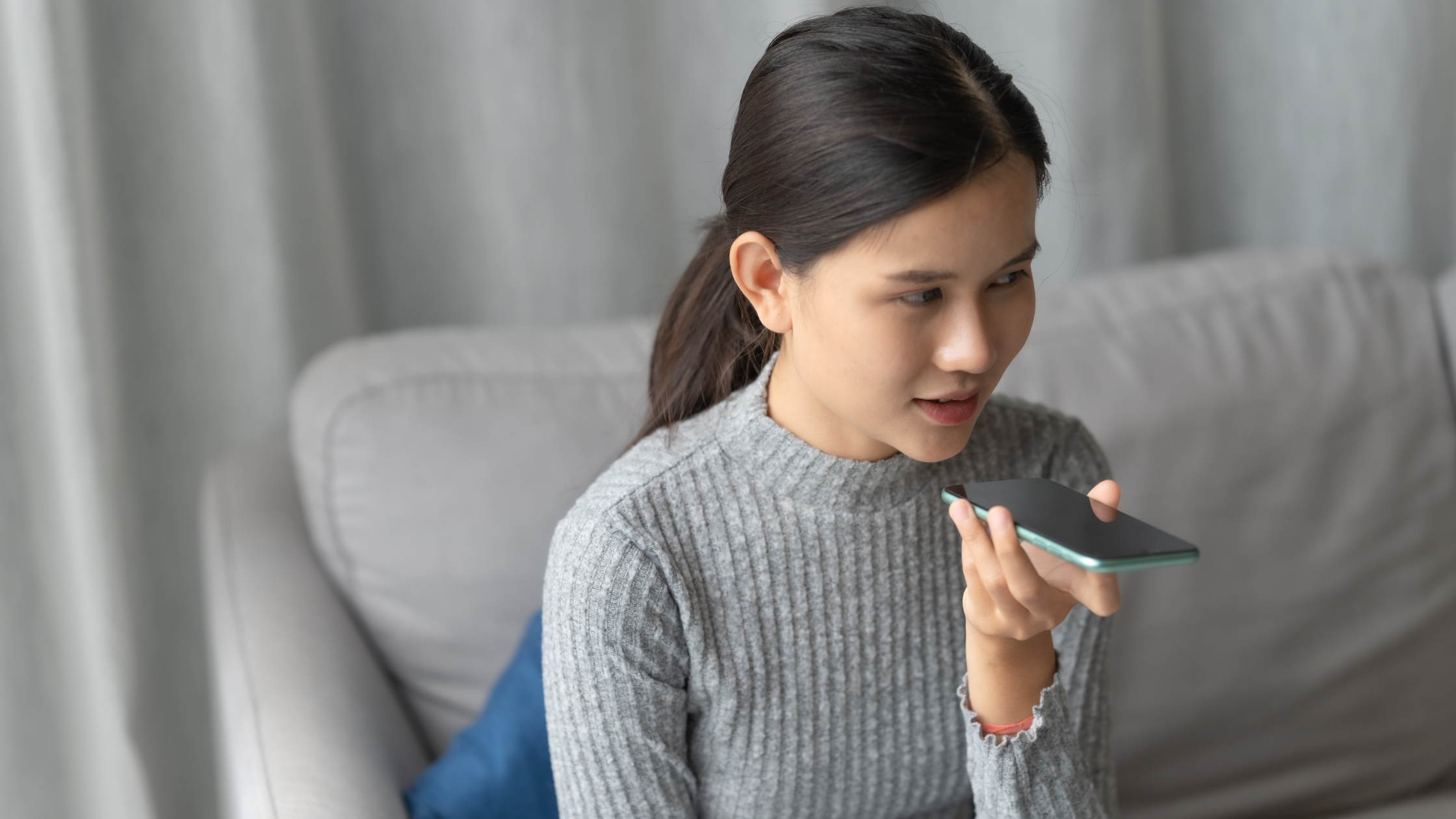 Woman using smartphone voice assistant at home speaking into device