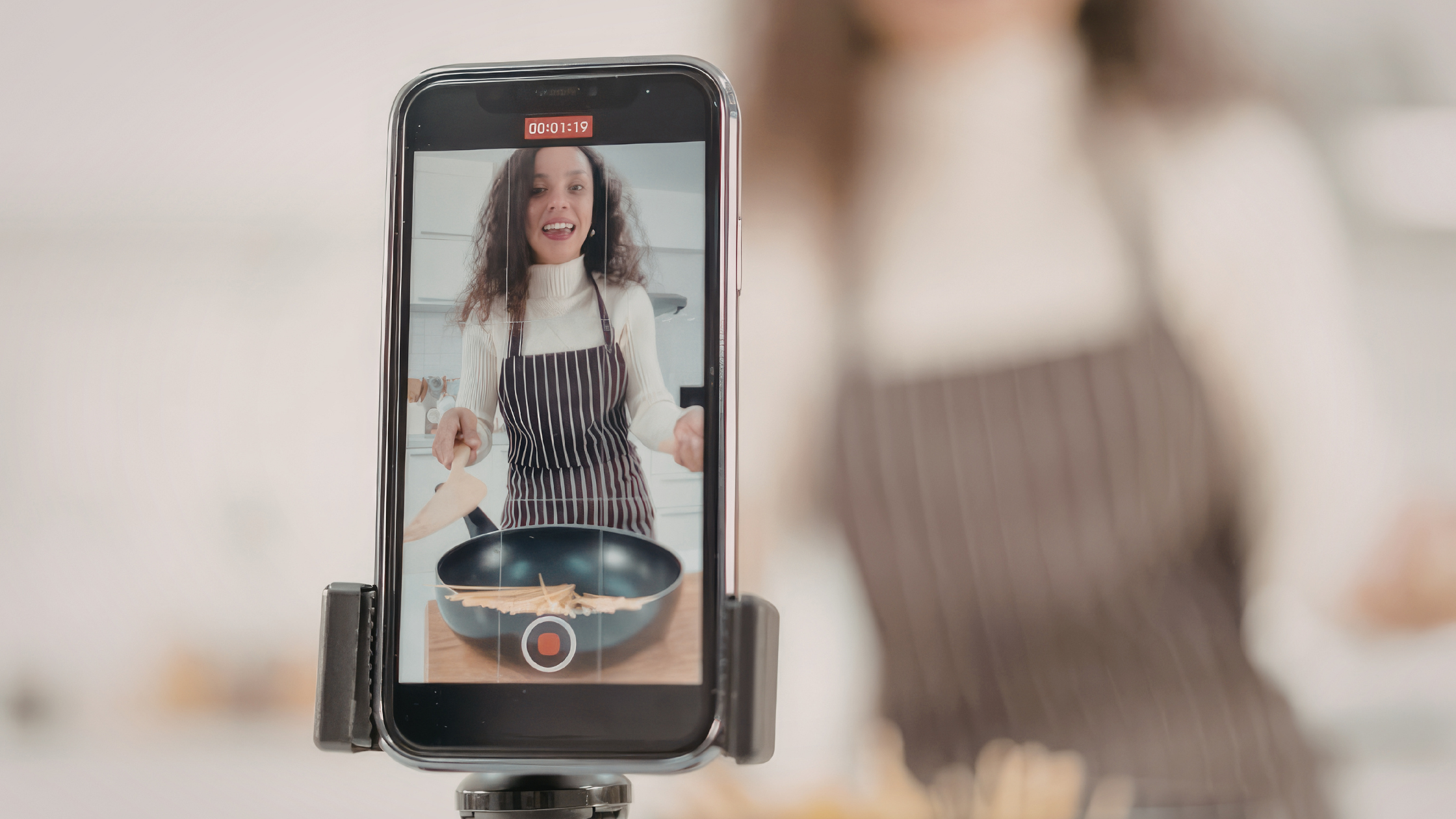Food and lifestyle creator recording smartphone video content in a kitchen for TikTok and Instagram.
