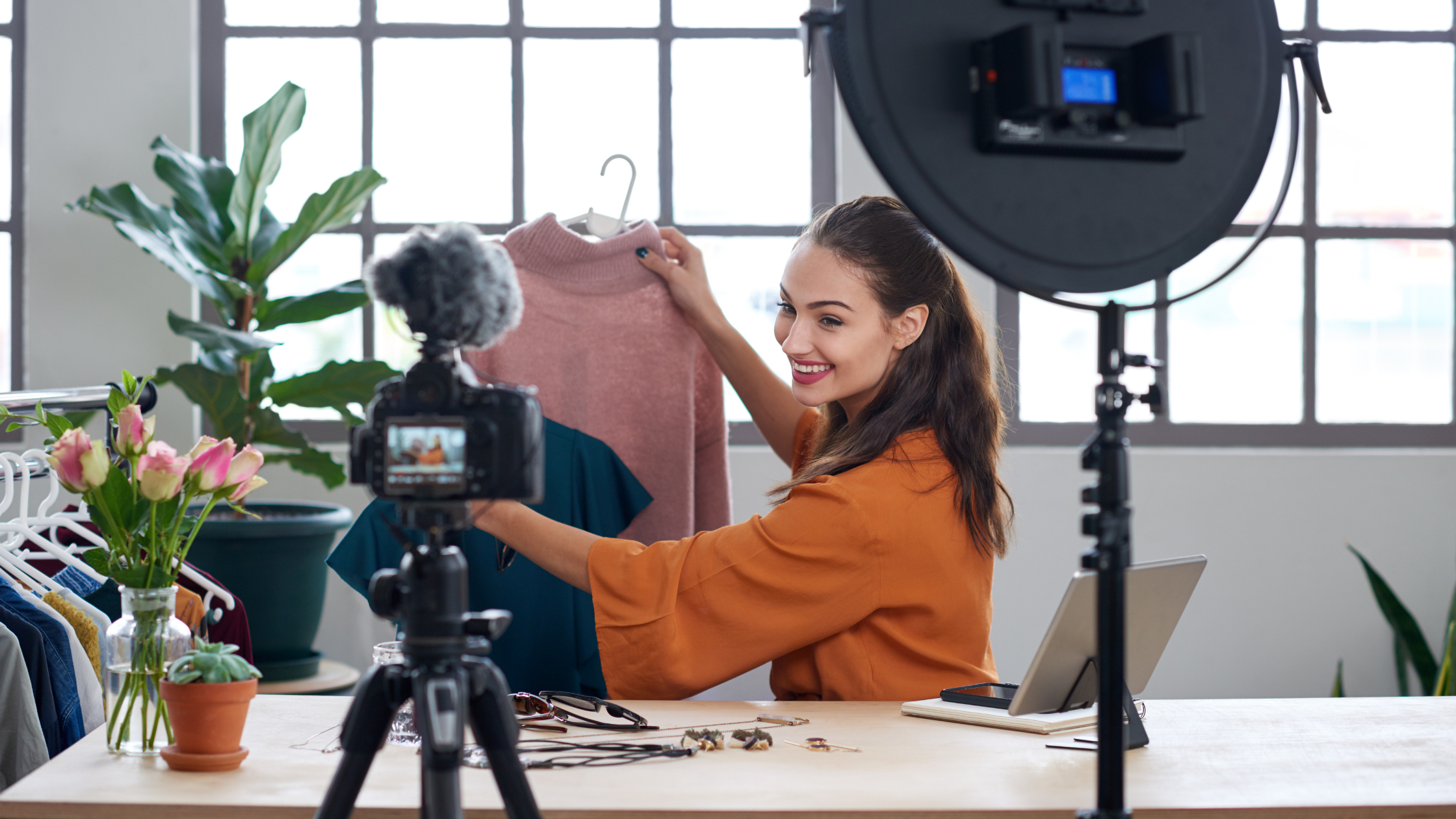 Fashion content creator filming product seeding video while holding pink sweater on hanger with camera and ring light