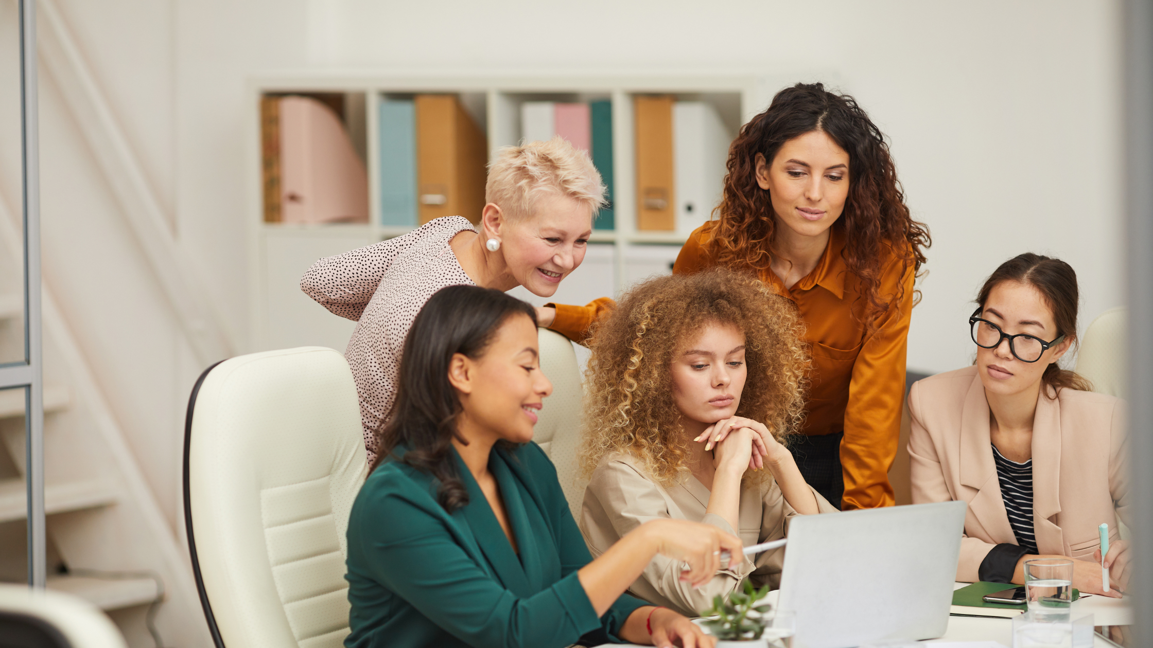 Diverse team of women reviewing product seeding strategy on laptop in bright office setting