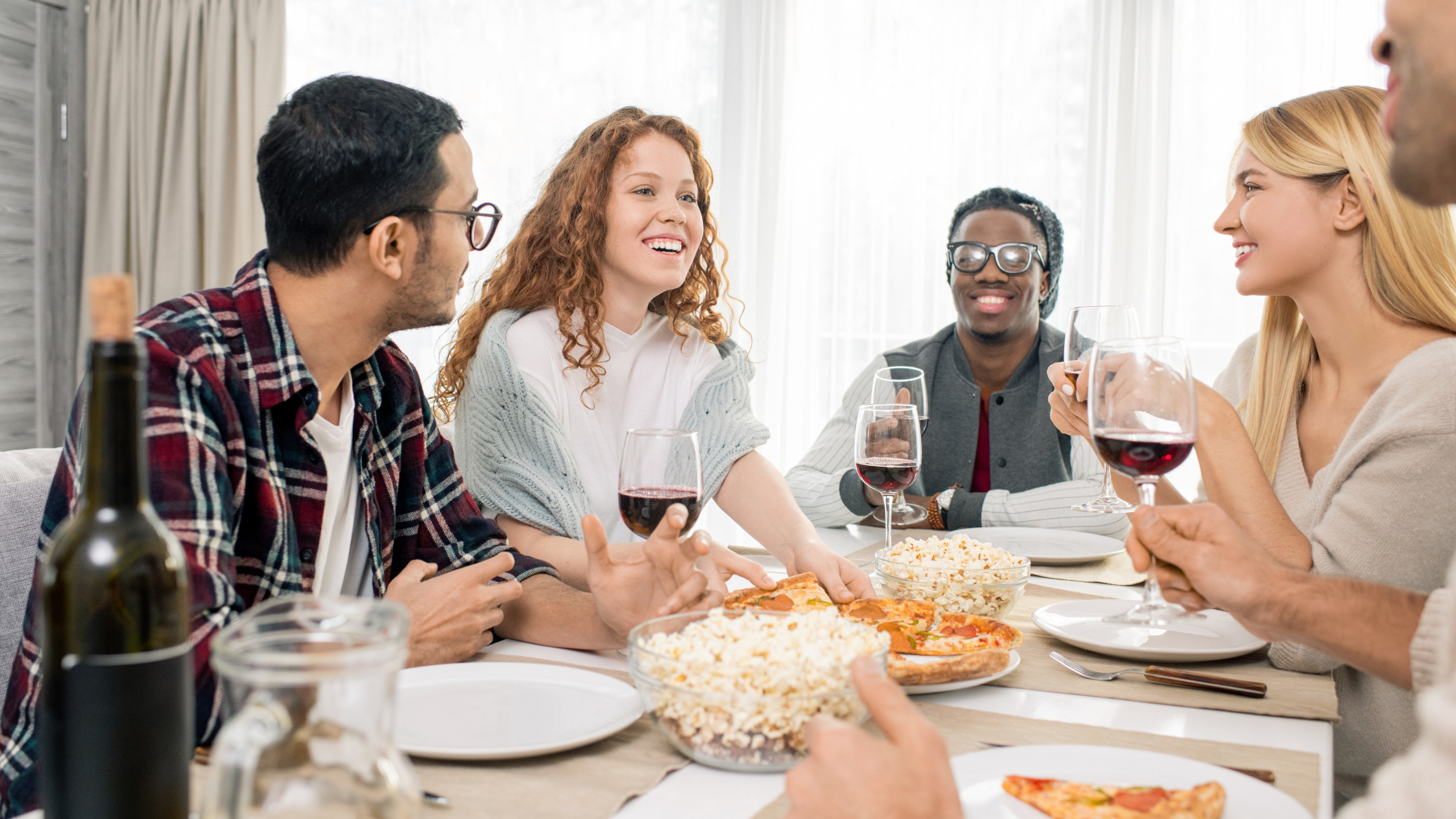 Diverse group of friends laughing and sharing food and wine at a dinner table, representing authentic peer-to-peer brand recommendations driven by micro influencer marketing and product seeding.
