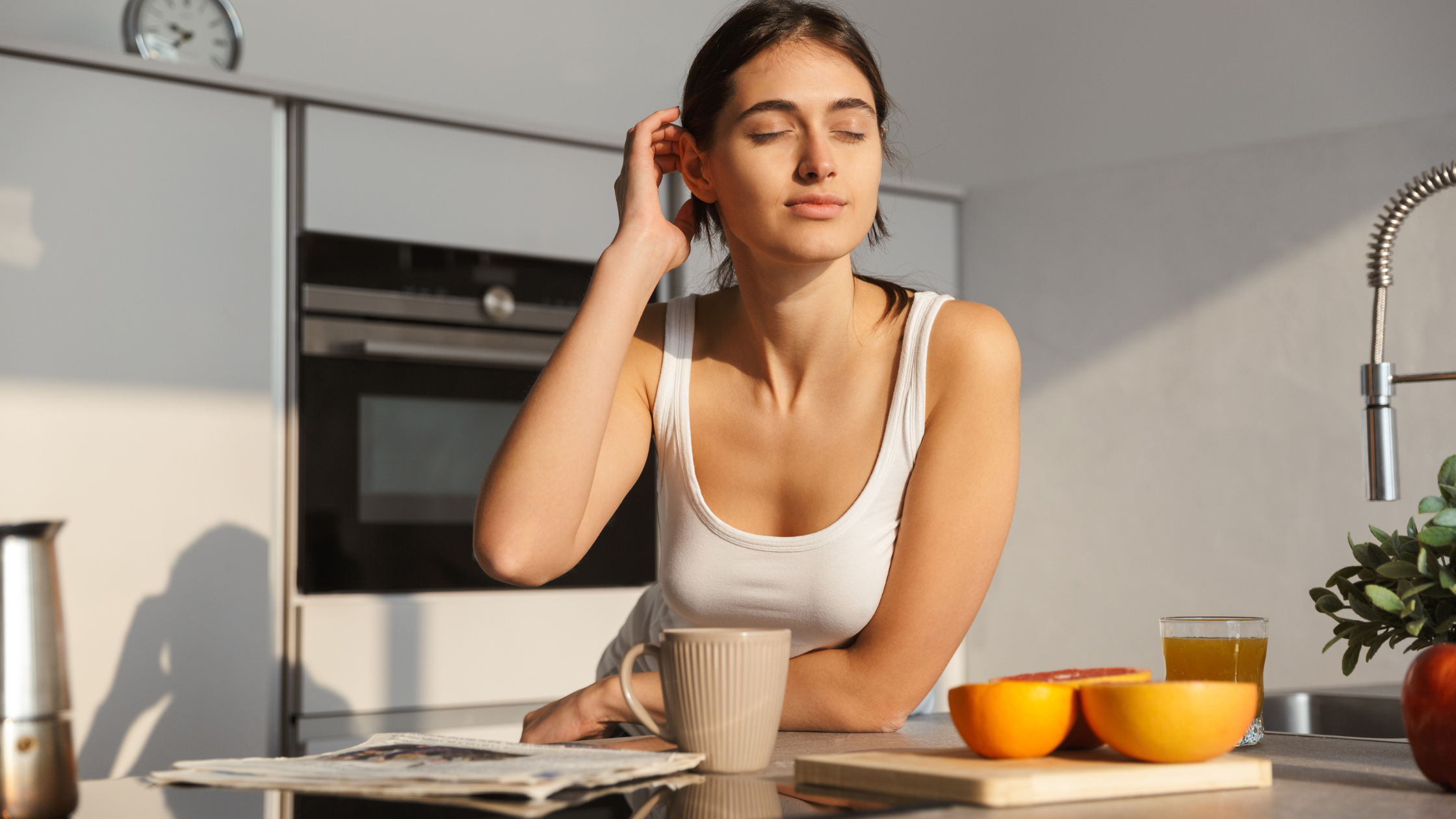 Young woman relaxing in a modern kitchen with a mug of coffee and fresh citrus fruit, representing the everyday lifestyle moments that product seeding campaigns capture through authentic creator content.