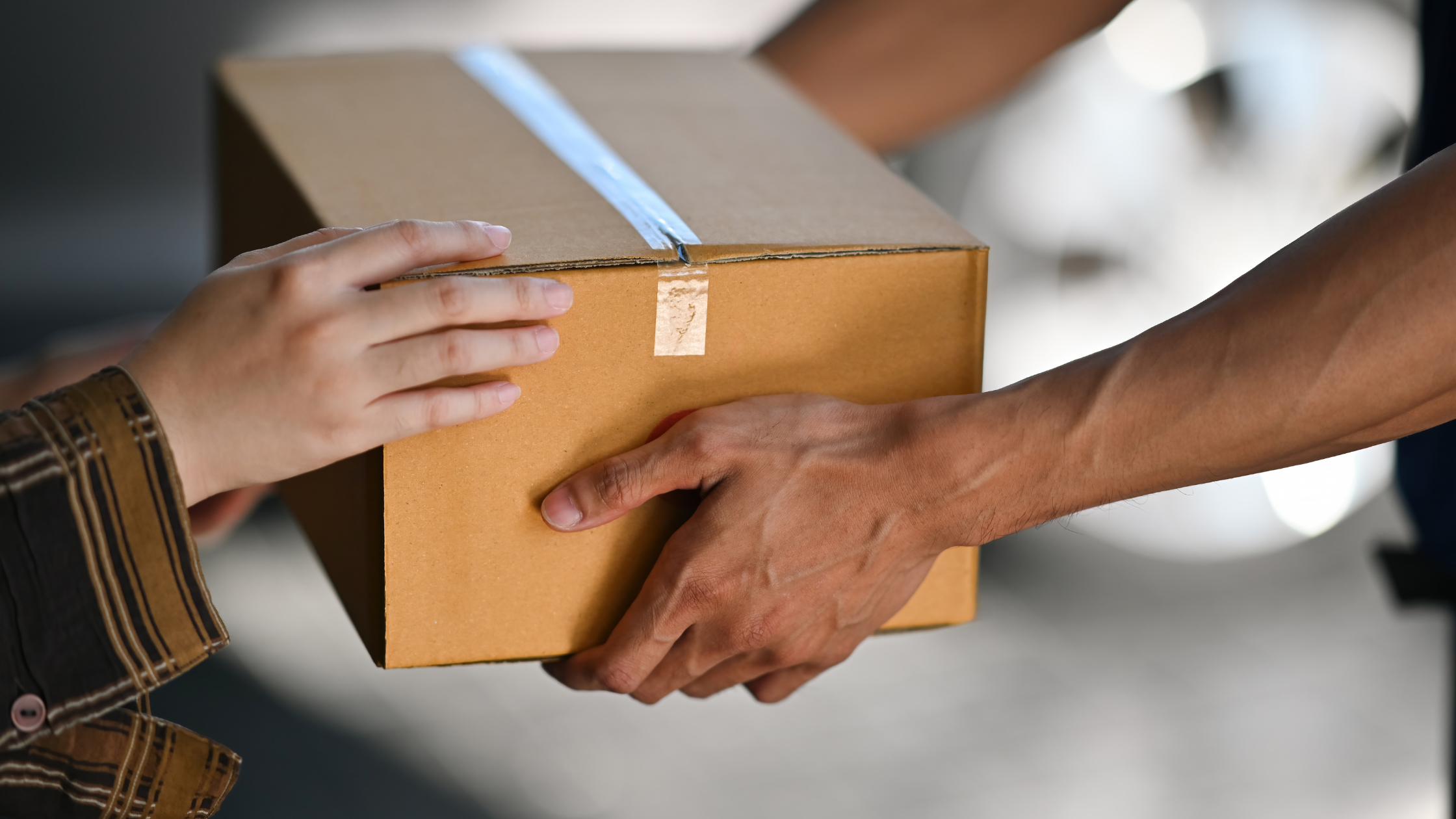 Two people exchanging a cardboard shipping box, representing the product seeding process where brands send free products to micro influencers and creators to generate authentic content and build brand awareness.
