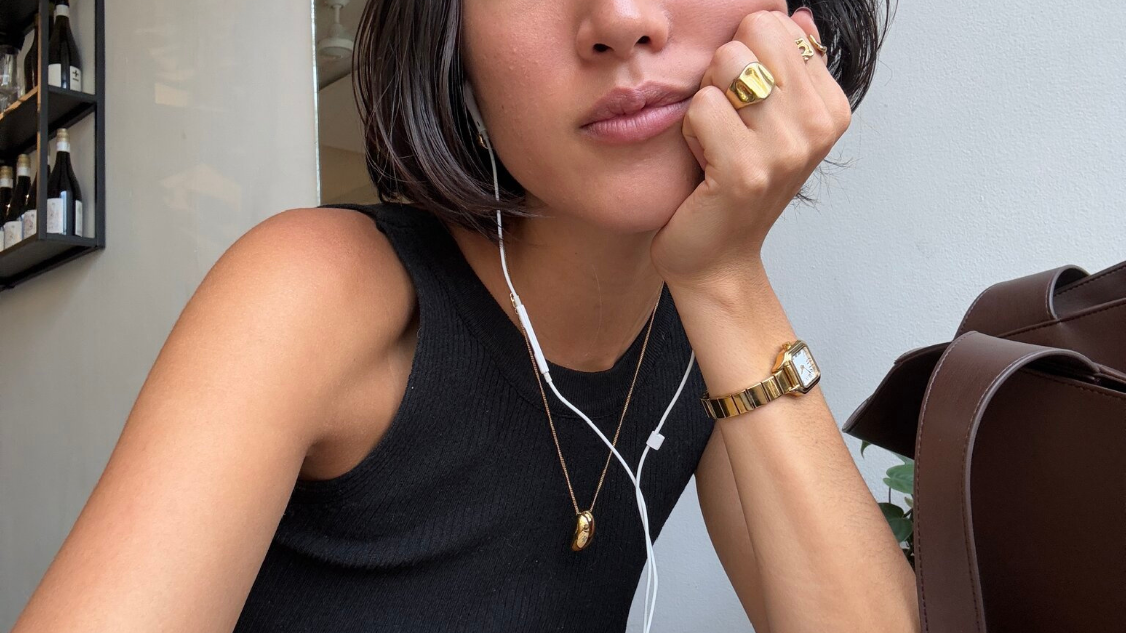Influencer wearing gold jewelry and earbuds, resting chin on hand in a lifestyle photo