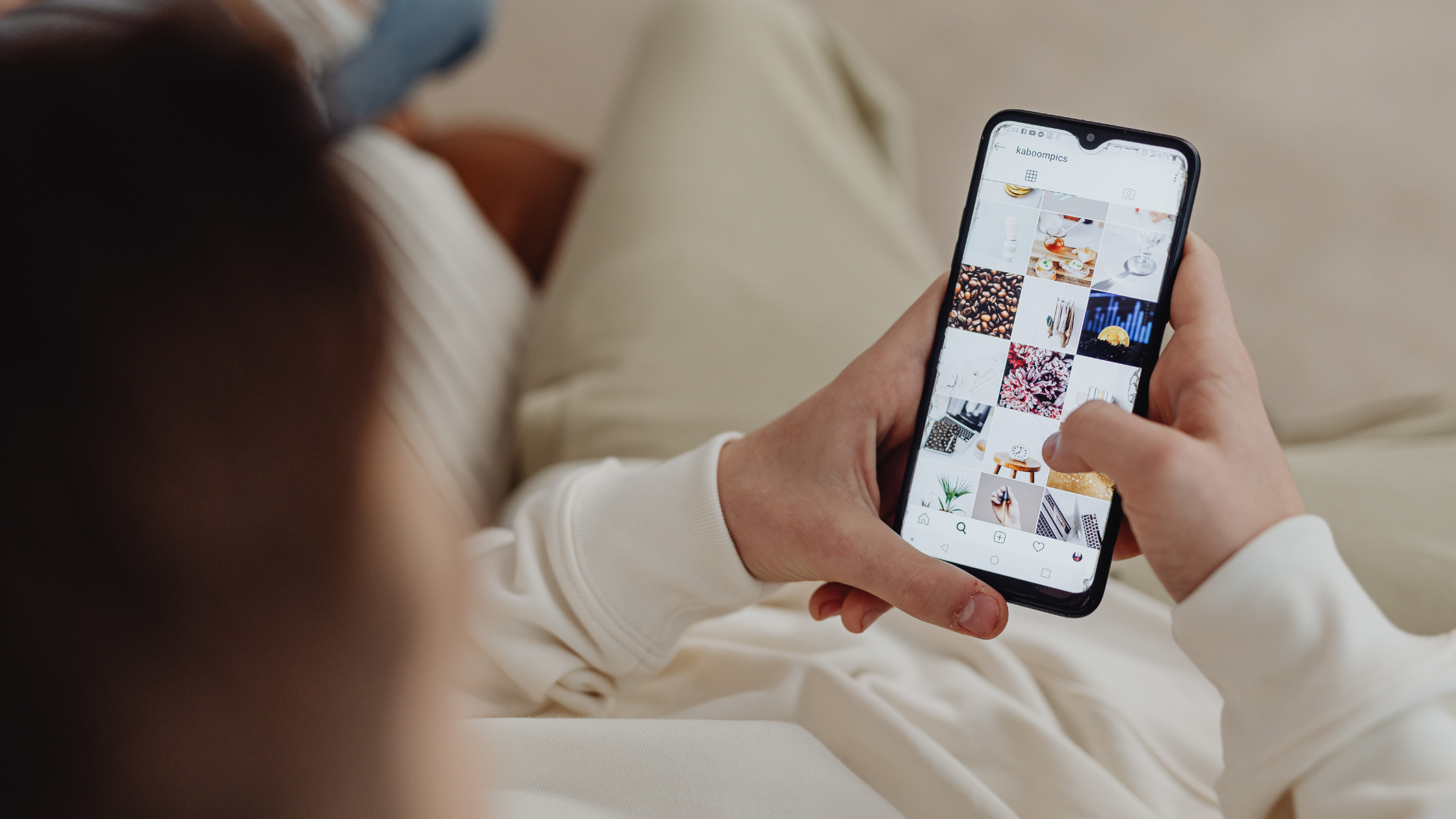 Person scrolling through an Instagram grid on a smartphone while sitting on a couch