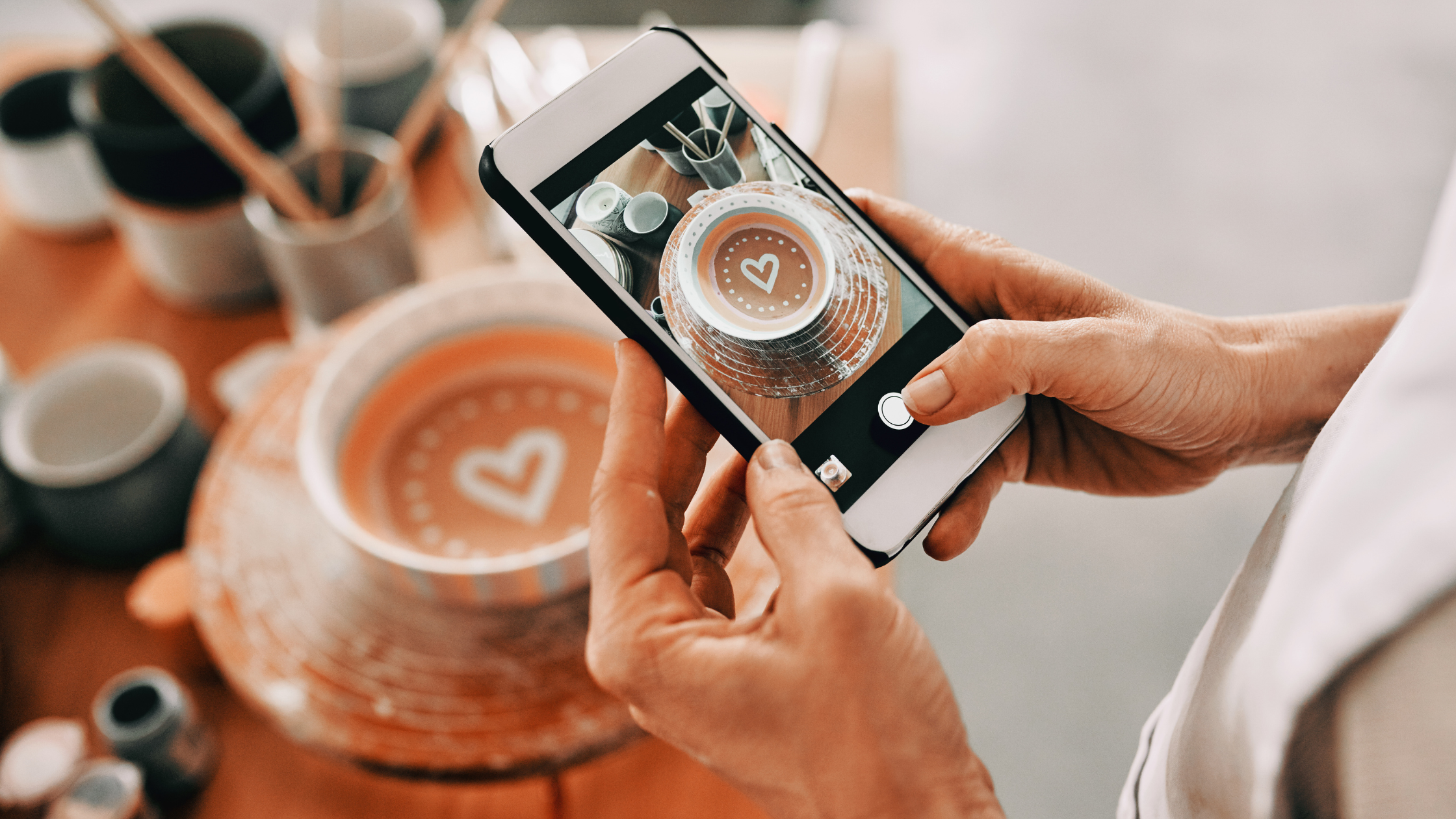 Hands photographing handmade pottery with a heart design for social content