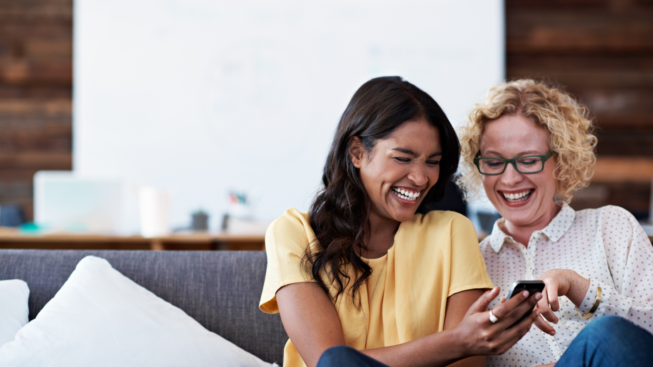 Two women laughing together while looking at a phone, representing genuine connection built through social media engagement
