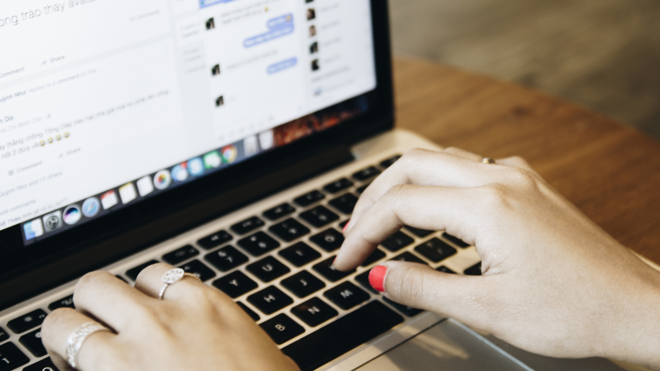 Hands typing on a laptop keyboard with a Facebook feed and comment thread open on the screen