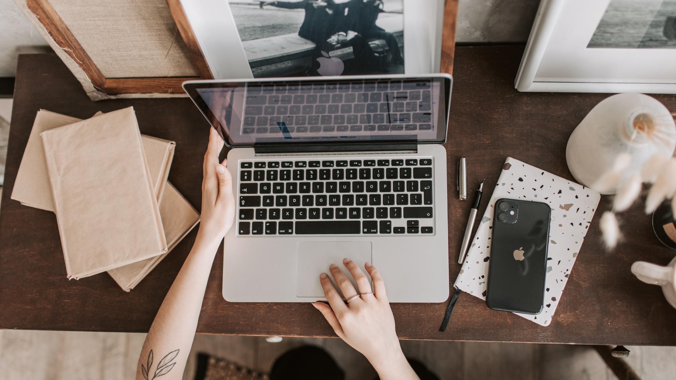 Overhead view of hands working on a laptop at a desk, representing the human strategy behind AI-assisted content creation