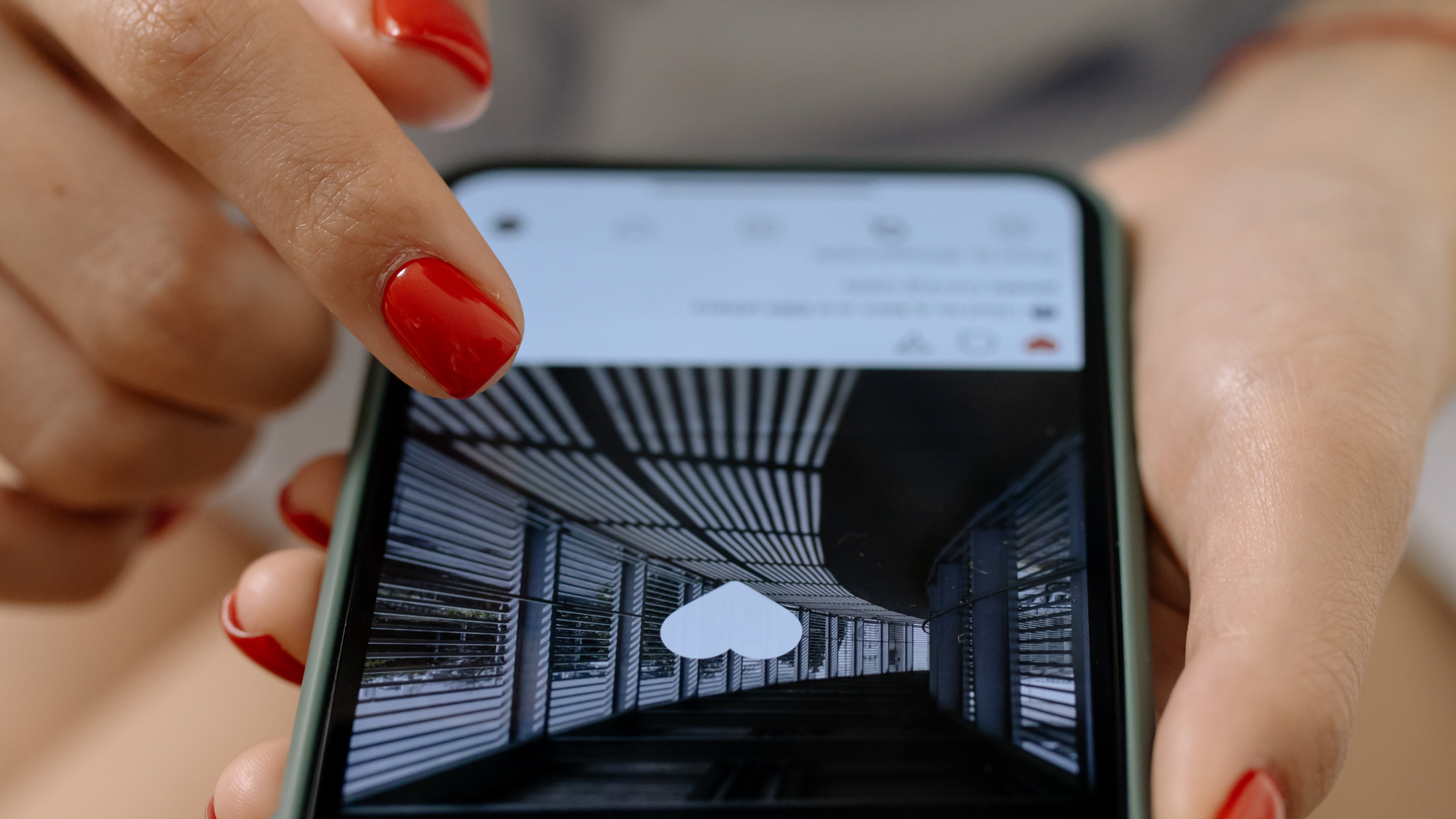 Hand with red nail polish double-tapping a phone screen to like a social media post, representing engagement and discovery