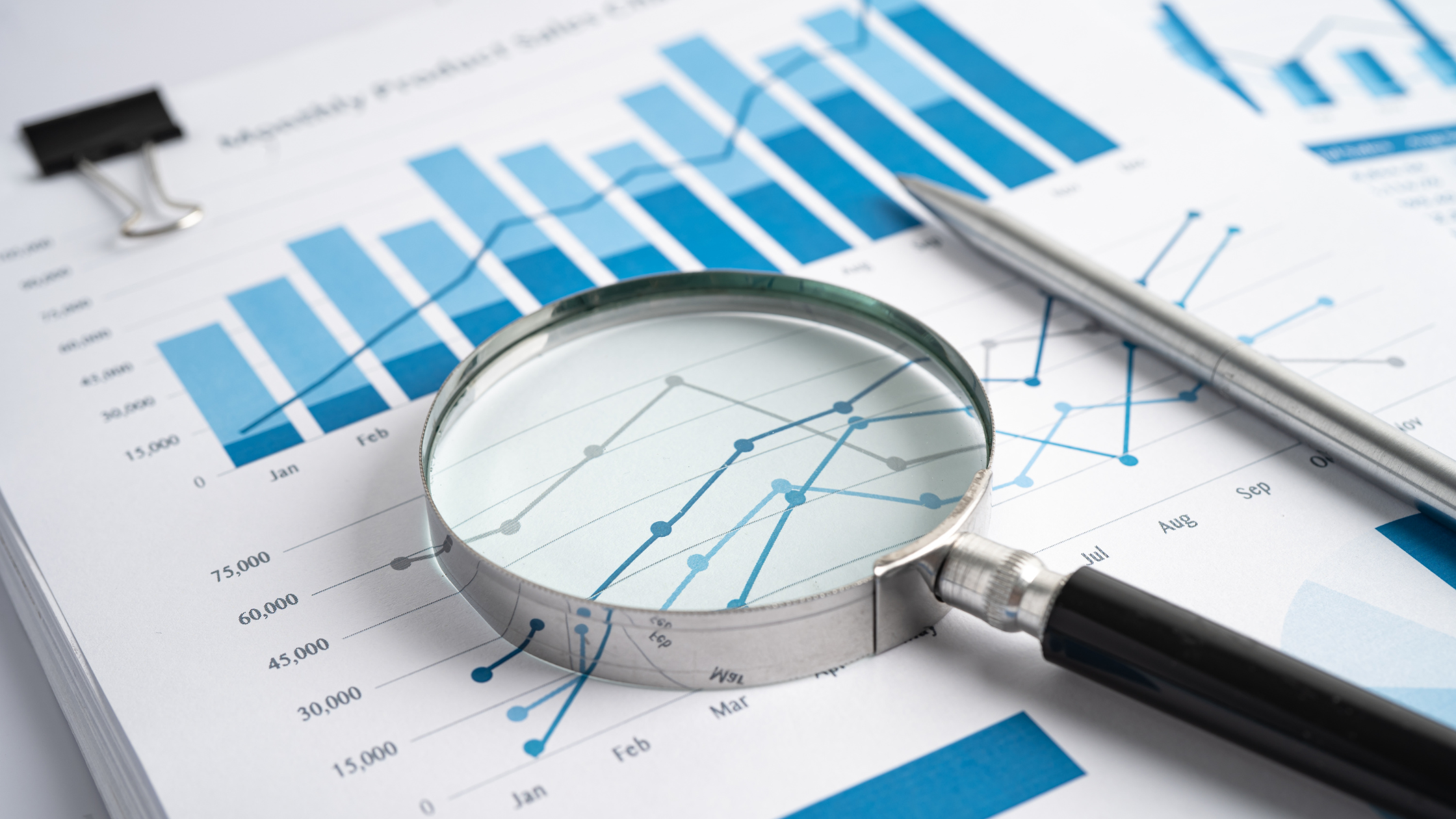 Magnifying glass resting on printed blue bar and line charts beside a pen, representing social media metrics that matter