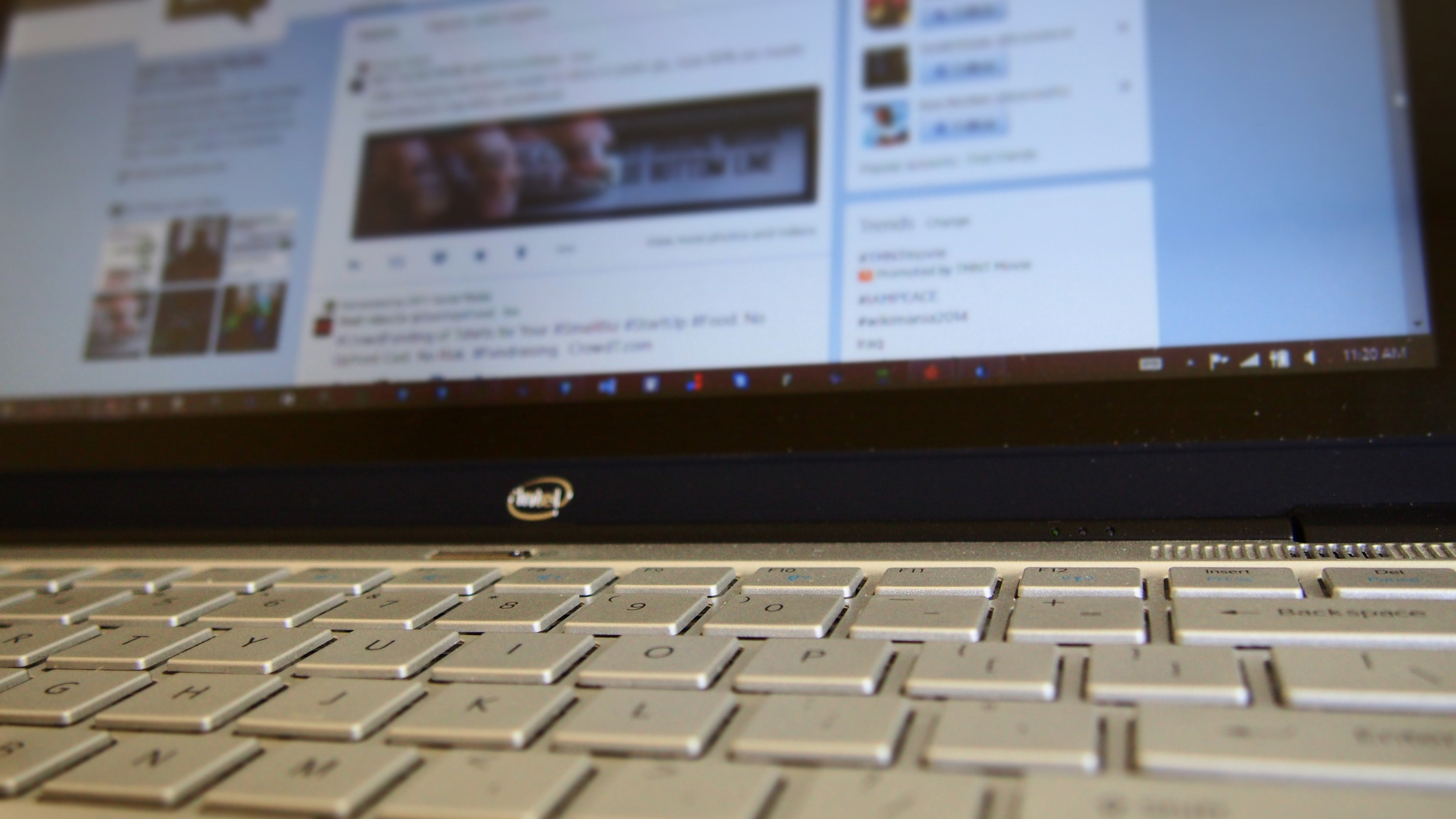 Close-up of a laptop keyboard with a social media feed and promoted trends blurred on the screen behind it