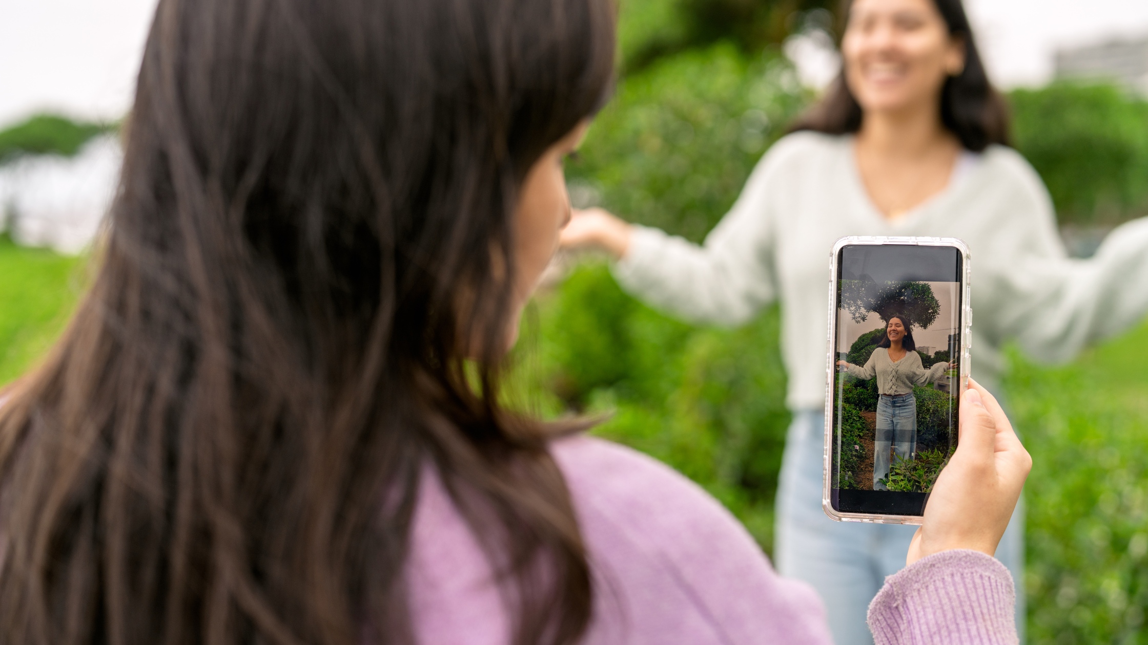 Woman filming a smiling friend on her phone outdoors in a garden, representing real, authentic social media content