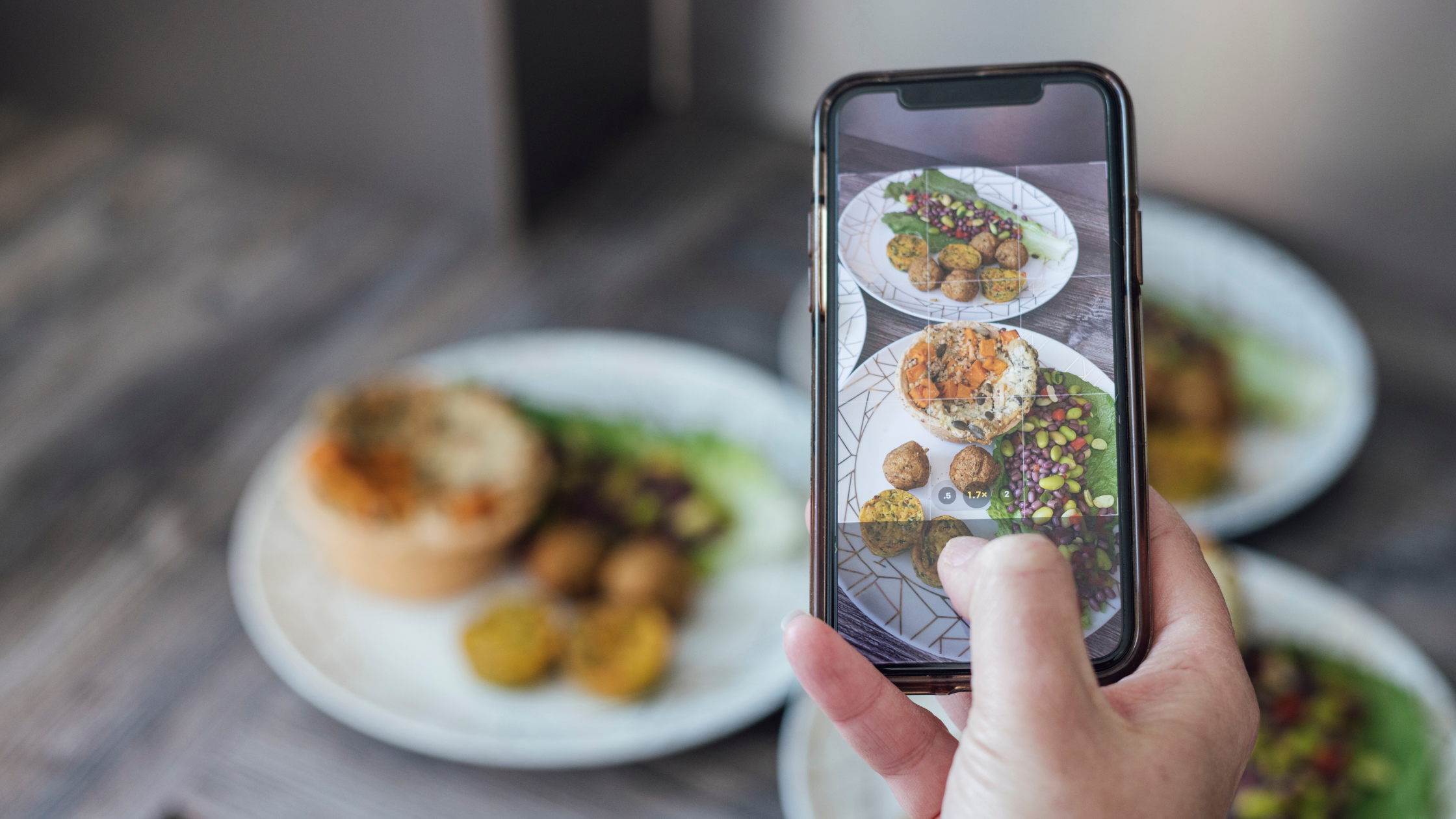 Phone showing an Instagram content grid next to a keyboard, laptop and camera, representing a business planning content like a media company