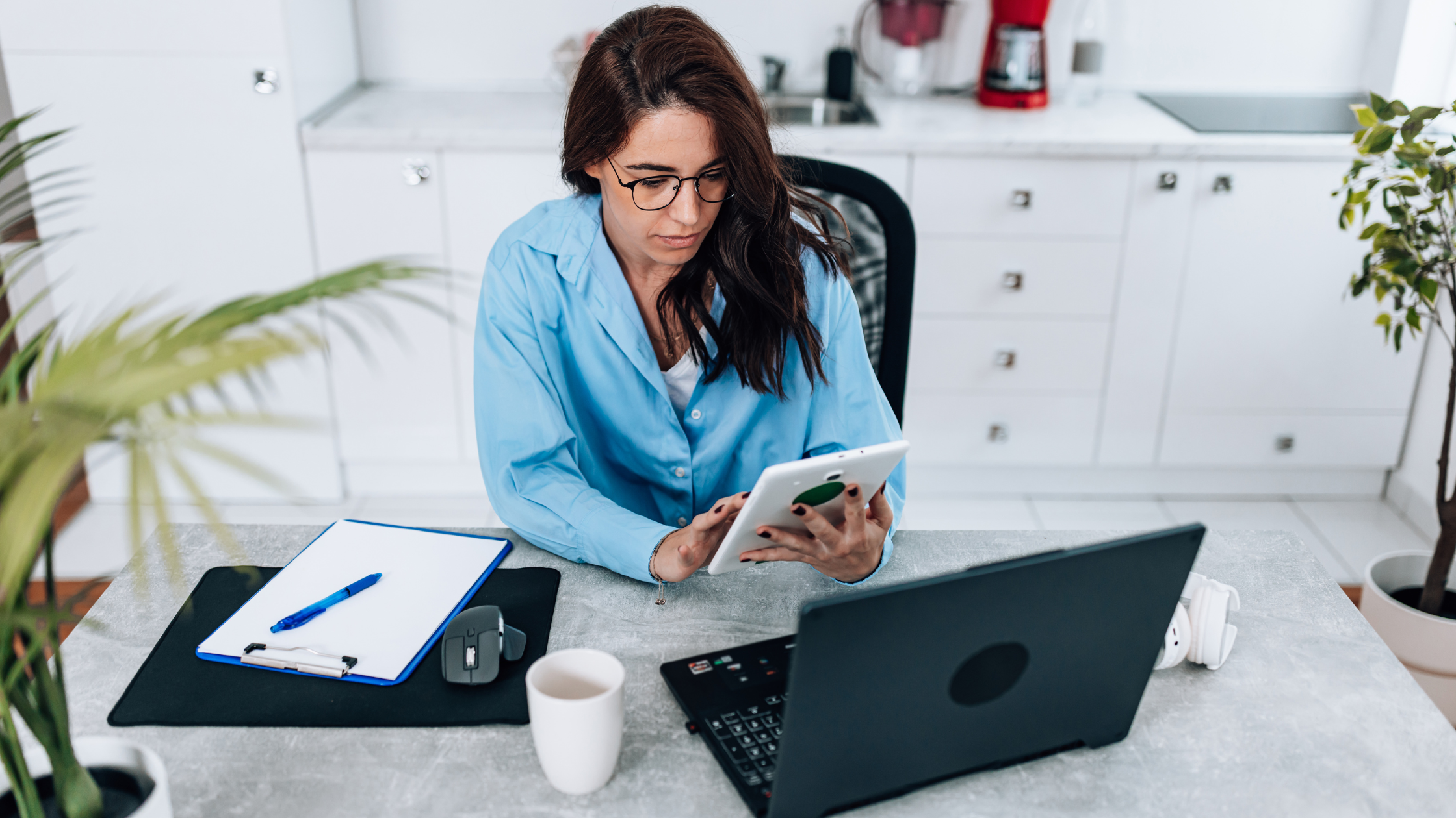 Business owner in a blue shirt reviewing results on a tablet at her desk, wondering why social media isn't driving sales